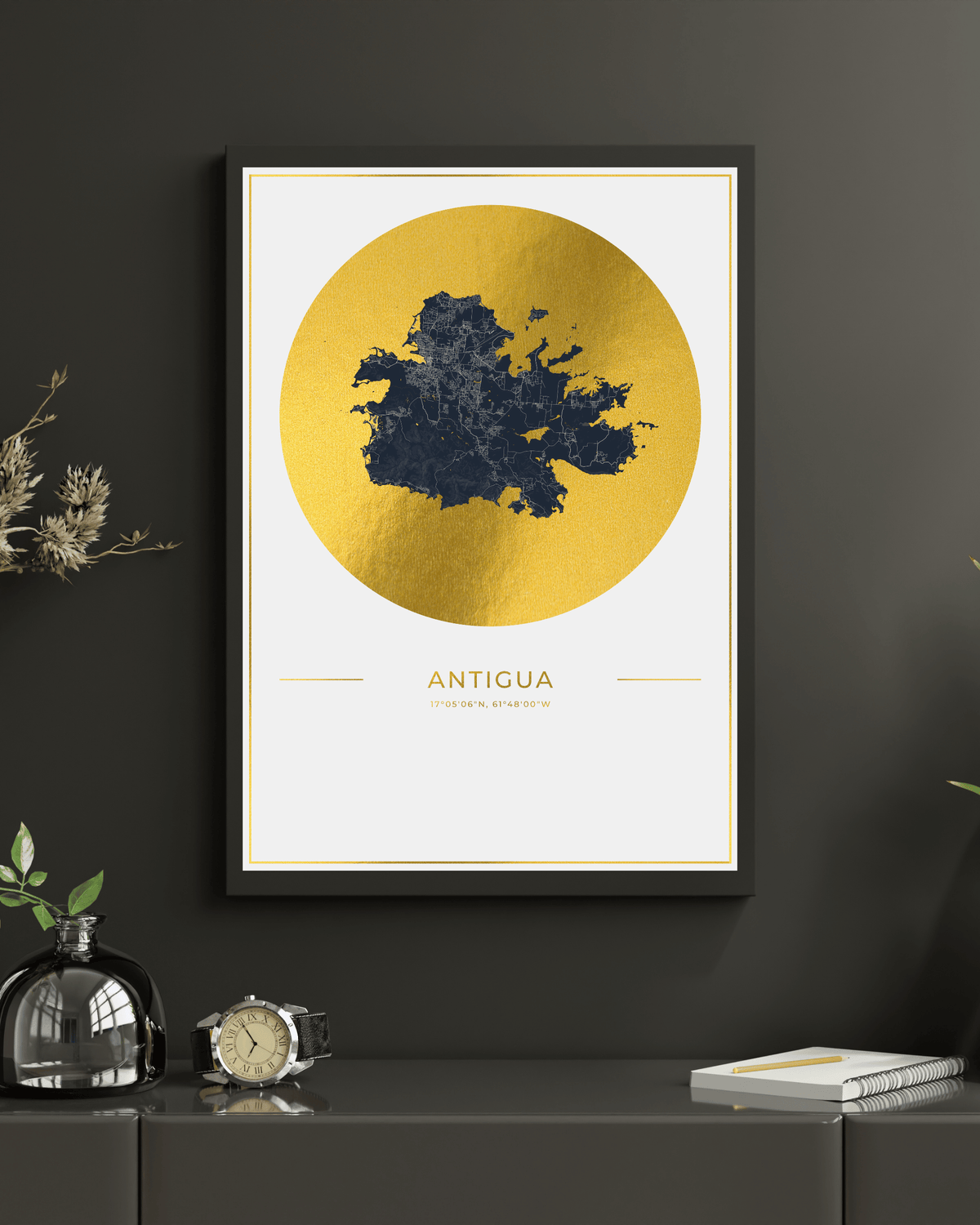 A framed wall art print featuring a gold circular map design labeled 'ANTIGUA' hangs on a dark charcoal wall above a console table with decorative objects.