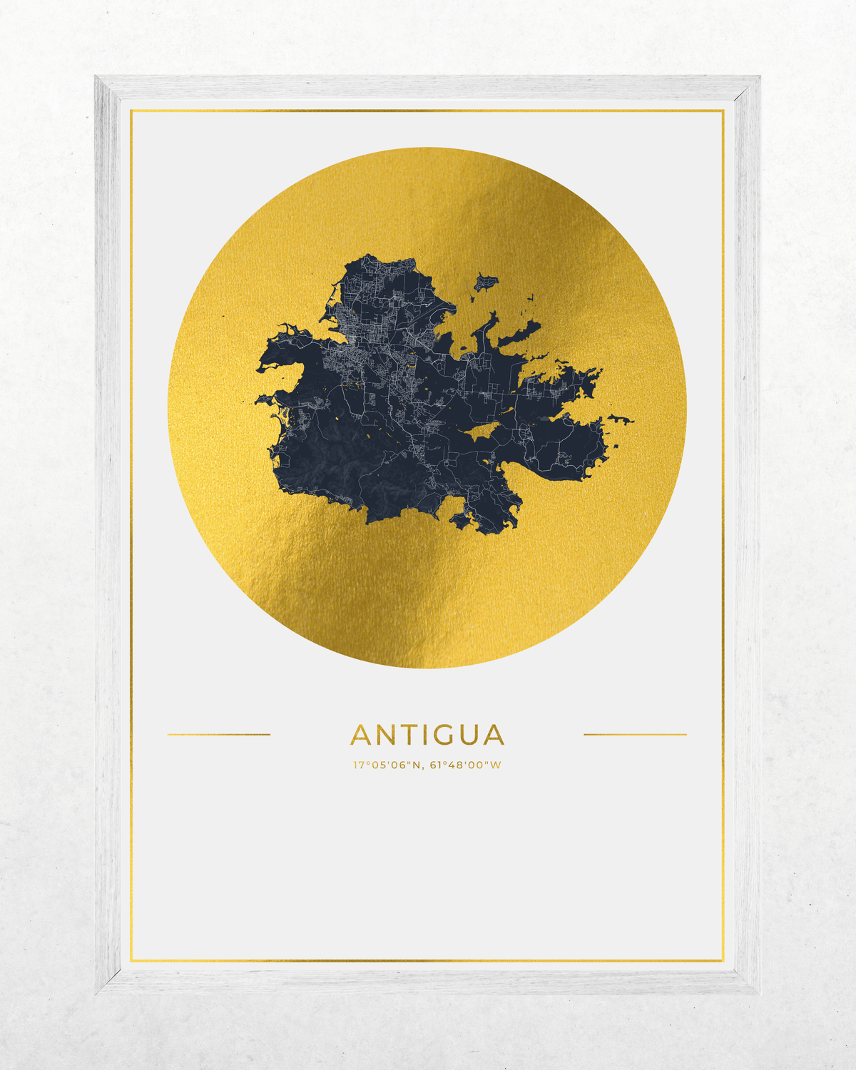 A framed art print featuring a dark navy blue map of Antigua over a large textured gold circle, with the word 'ANTIGUA' printed below in gold, set in a white frame against a light textured background.
