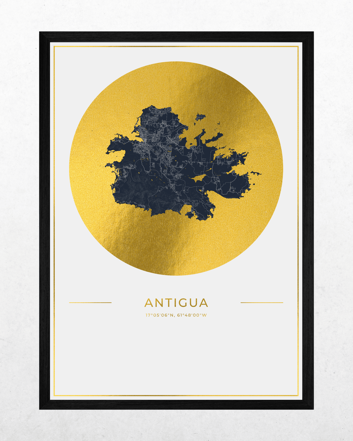 A framed art print featuring a dark navy blue map of Antigua over a large textured gold circle, with the word 'ANTIGUA' printed below in gold on a white background, enclosed in a black frame.