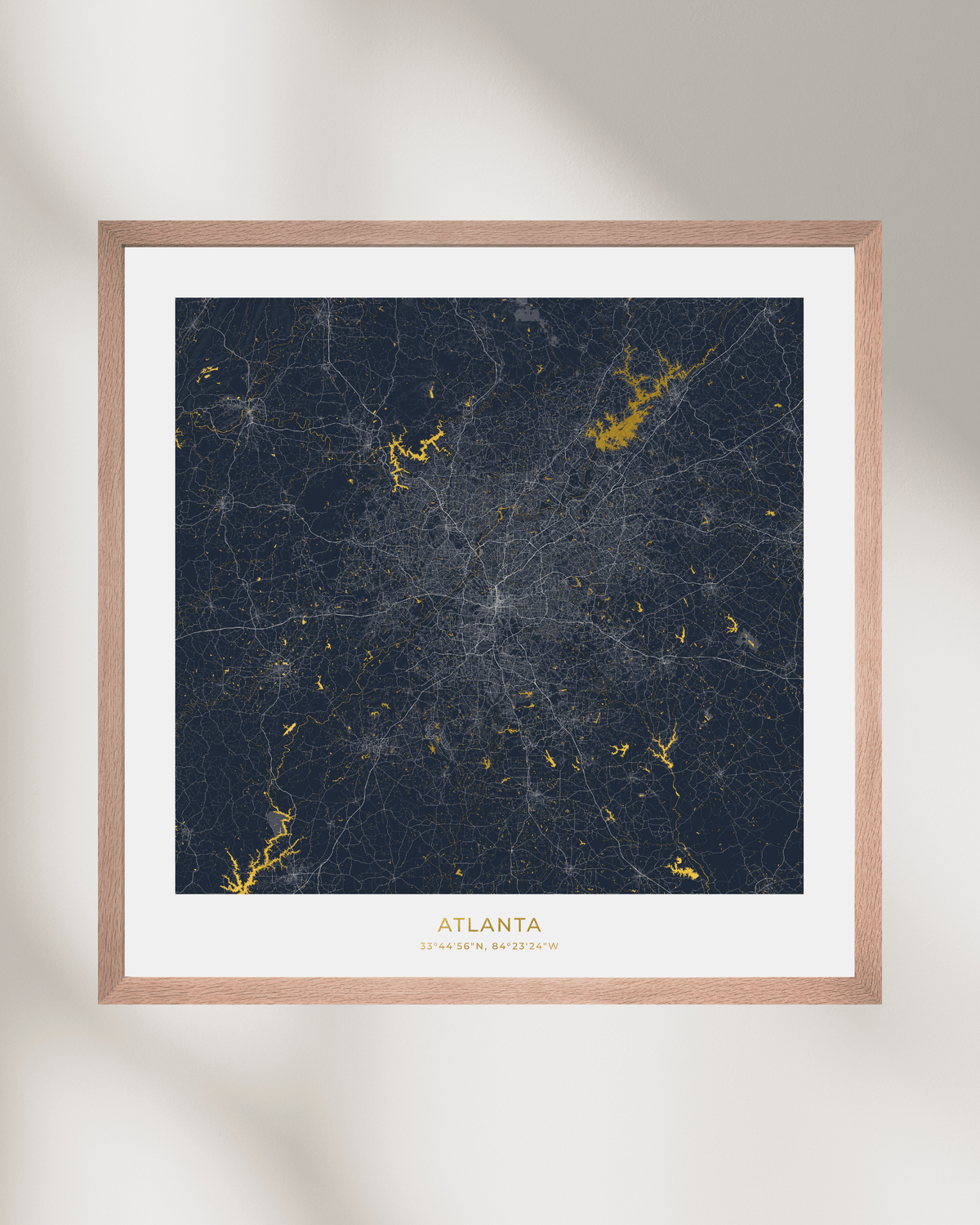 Framed modern city map print of Atlanta, Georgia, featuring a dark navy blue street network with gold waterways & lakes , set in a light wood frame with a white mat.