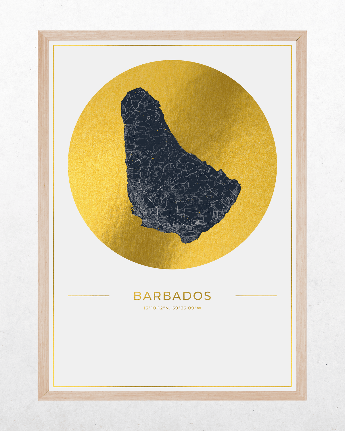 A framed art print featuring a stylized map of Barbados in dark blue set against a metallic gold circular background. The print is housed in a light natural wood frame and displayed on a textured off-white wall.