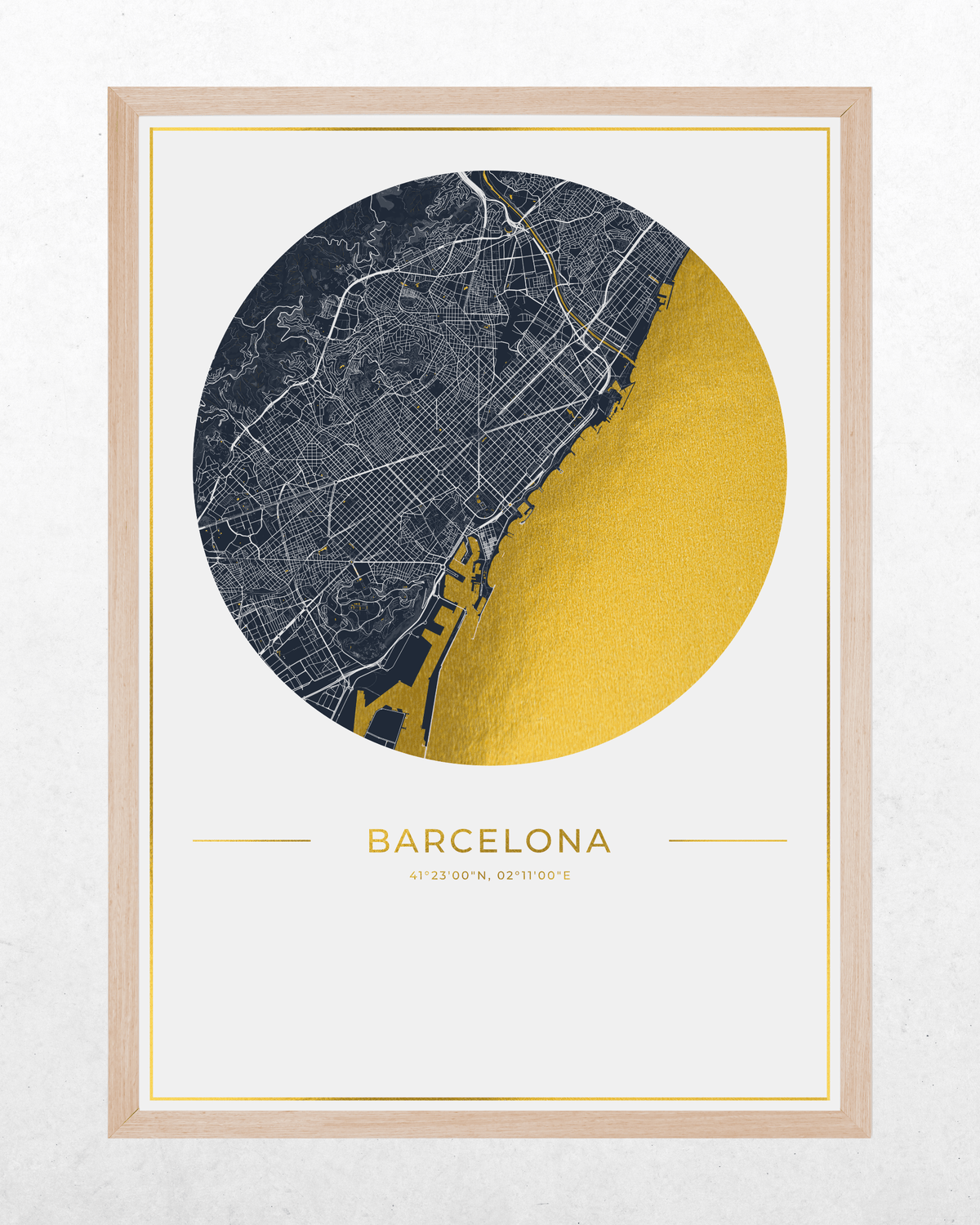 A framed minimalist city map print of Barcelona, featuring a circular graphic with a dark navy street grid and a large textured gold section, with the word BARCELONA and coordinates below, set in a light wood frame against a white wall.