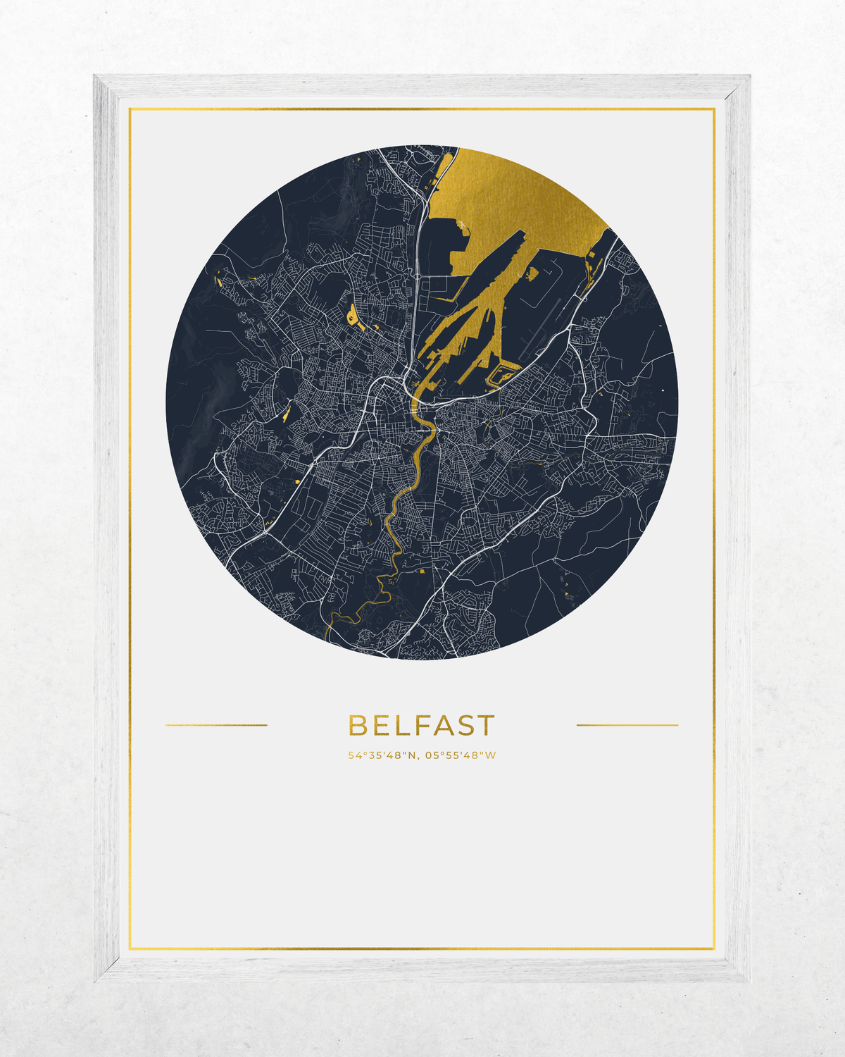 A framed minimalist map print of Belfast, featuring a circular dark navy and gold city layout on a white background with the word 'BELFAST' and coordinates printed below, set in a light wood frame.