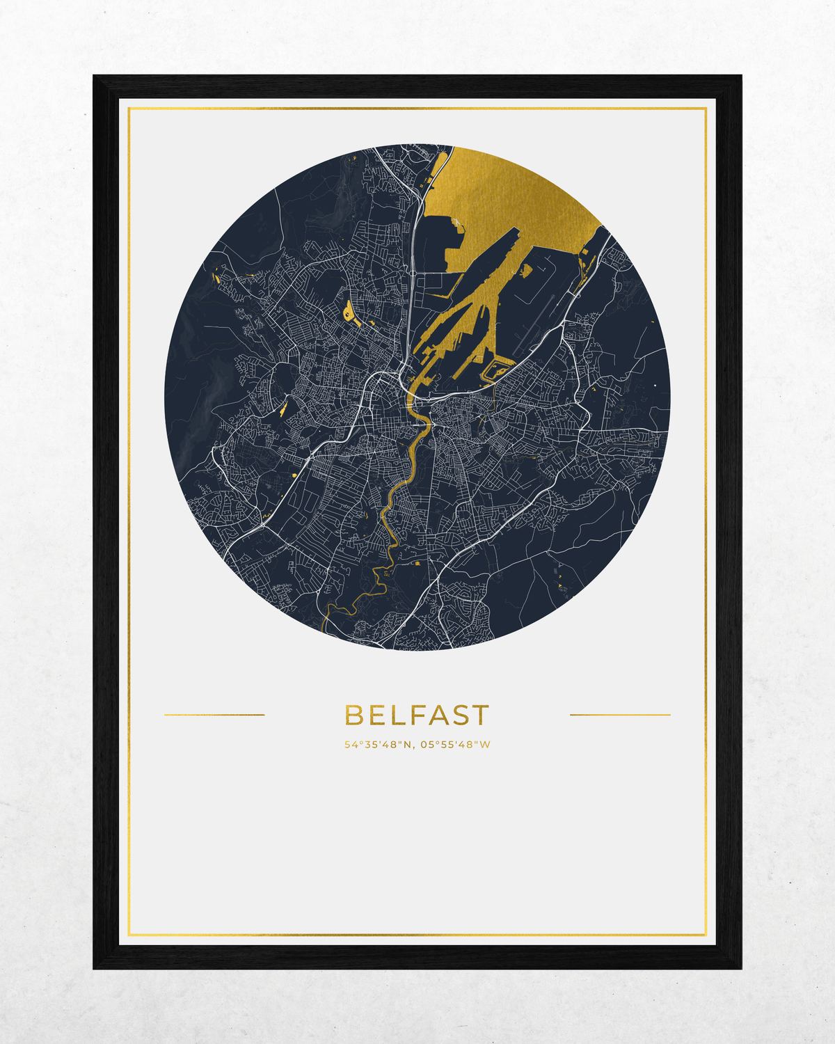 A framed city map print of Belfast, Ireland, featuring a circular dark navy map with gold river and coastline highlights, a white mat, and a black frame on a light textured background.