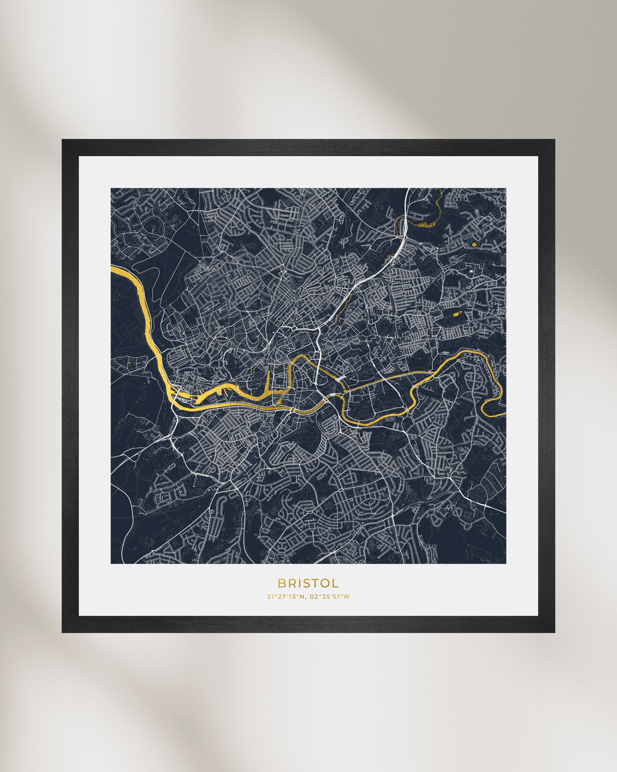 Framed city map print of Bristol, UK, featuring a dark navy street grid with white lines and a highlighted gold River Avon, presented in a black frame with a white mat.