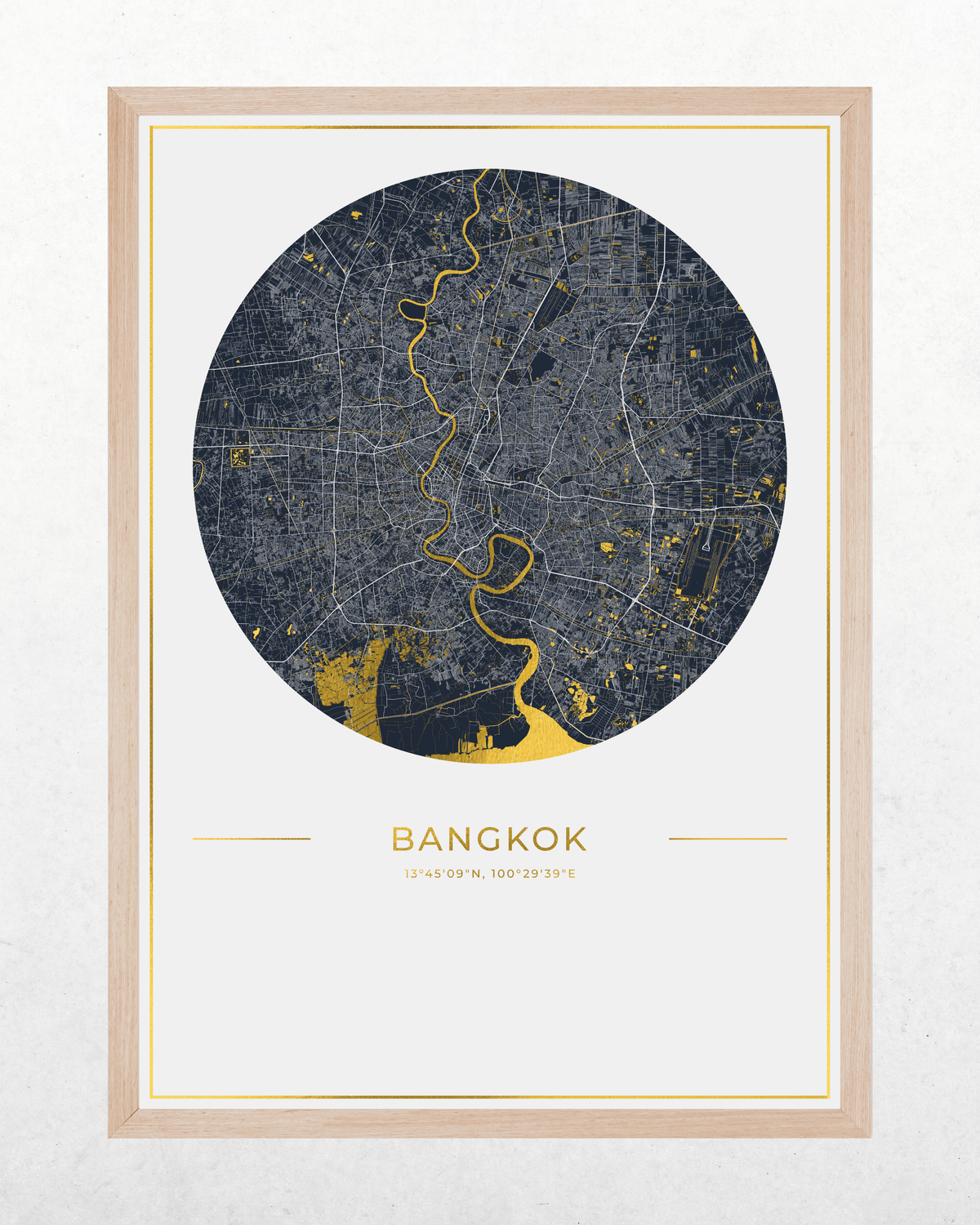 A framed circular map print of Bangkok, Thailand, featuring a dark gray street layout with gold highlights and the city name printed below, shown in a light wood frame against a white wall.