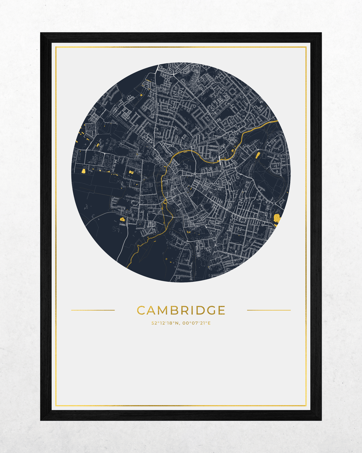 A framed circular city map print of Cambridge, UK, featuring a dark navy street network with gold line details on a white background, with the word 'CAMBRIDGE' and smaller text below, shown in a black frame against a light textured wall.