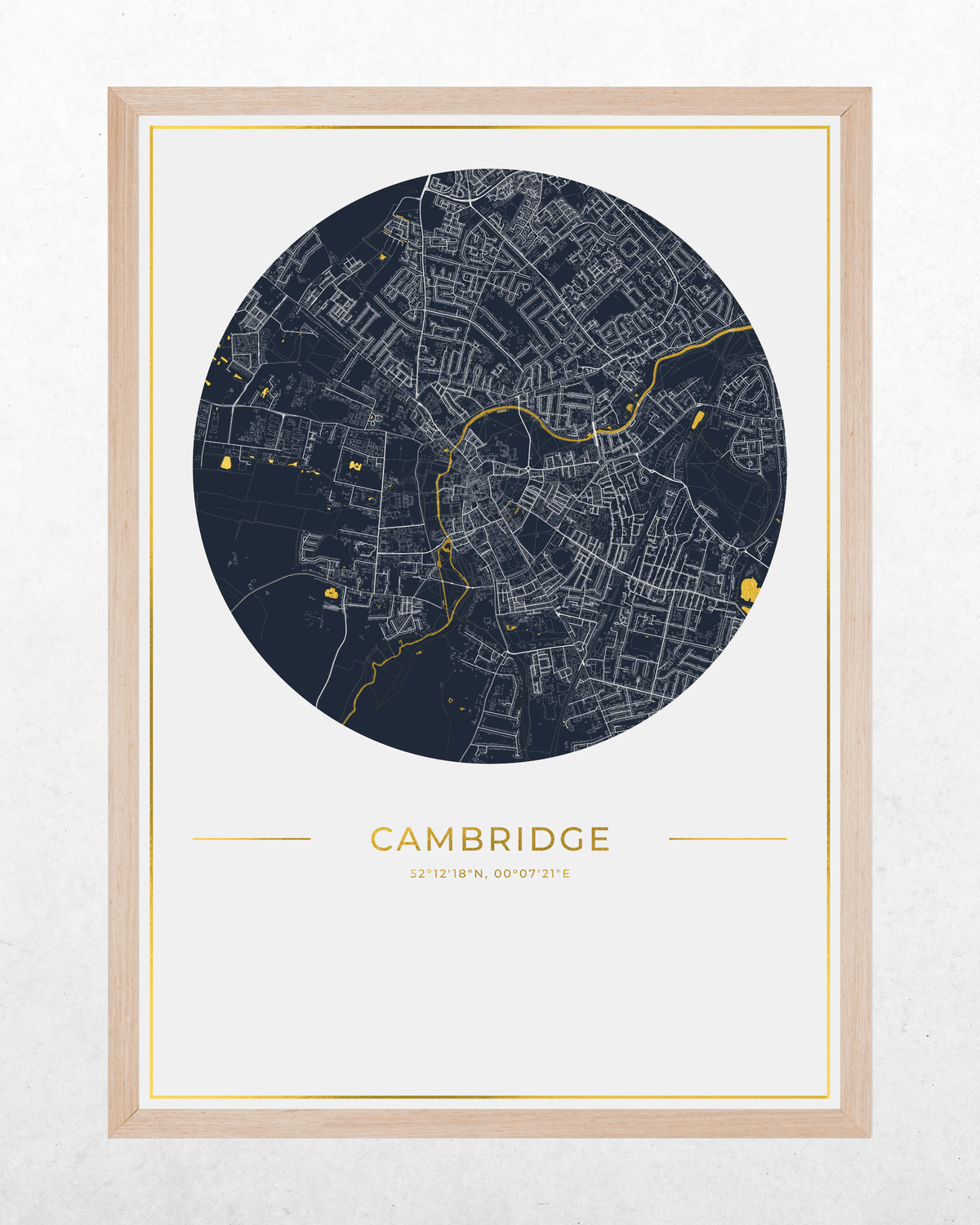 A framed circular city map print of Cambridge, UK, featuring a dark navy street network with gold line details and the word 'CAMBRIDGE' in gold below, set in a light wood frame against a white background.