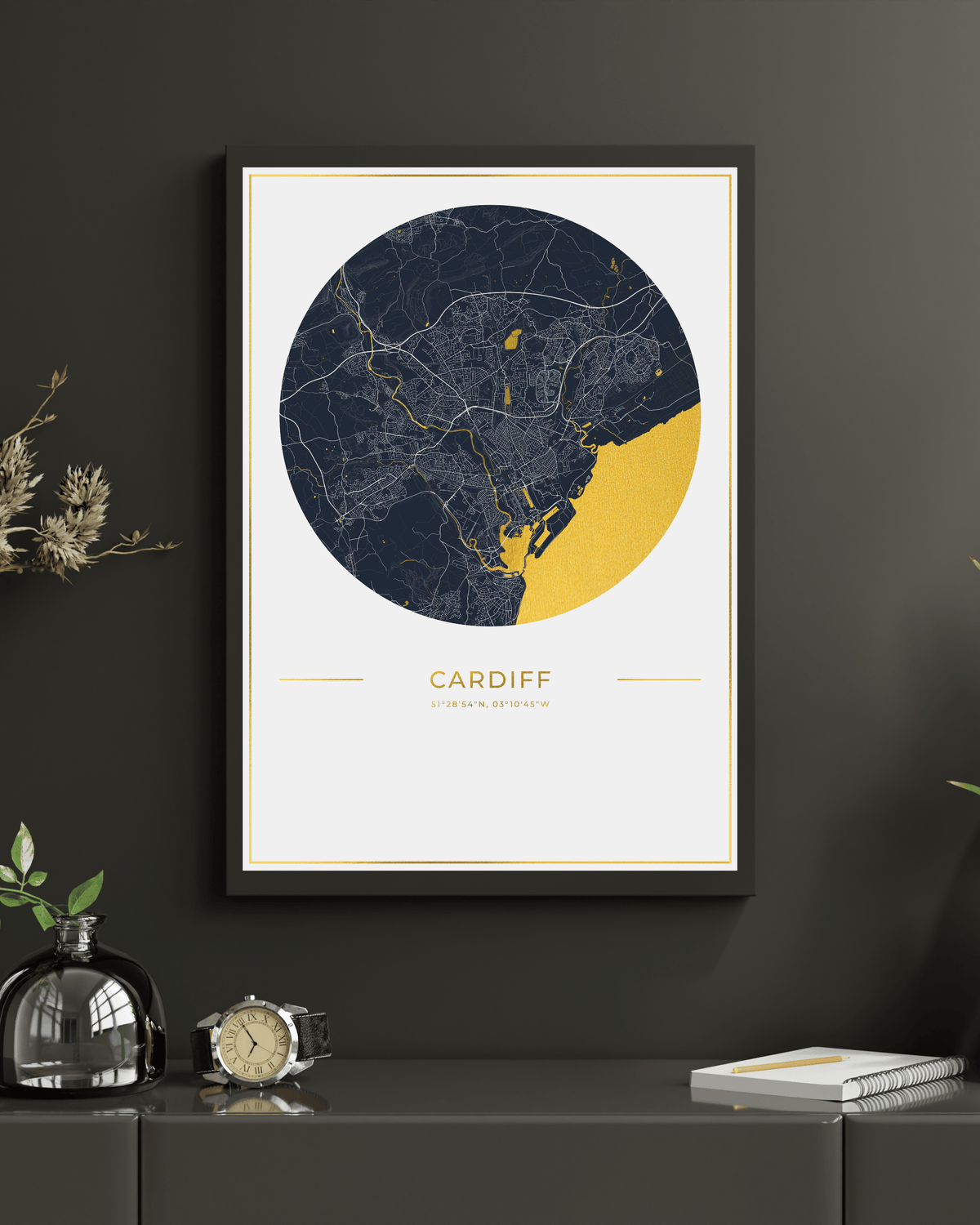 A framed circular city map print of Cardiff, Wales, displayed on a dark gray wall above a console table. The print features a navy blue and yellow map design with gold accents and the word 'CARDIFF' printed below.