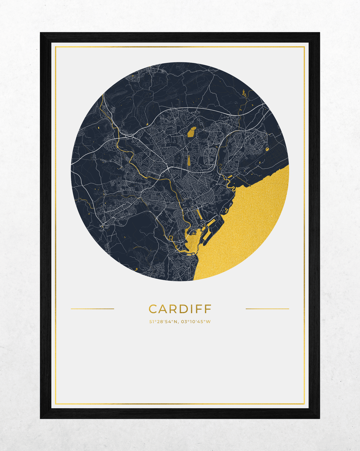 A framed city map print of Cardiff, Wales, featuring a dark navy circular map with fine white street lines and a gold foil highlights, set in a black wood frame on a white background.