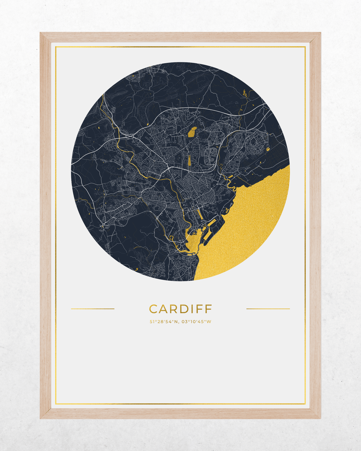 A framed city map print of Cardiff, UK, featuring a circular navy and gold map design on a white background with a light wood frame.