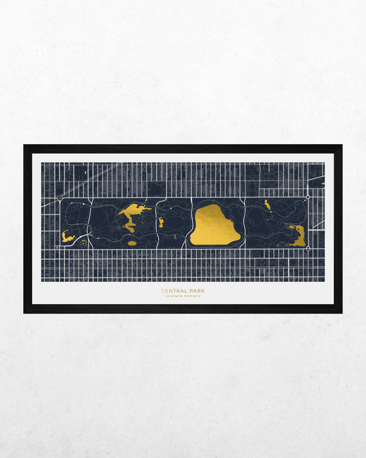 A framed horizontal map print of Central Park, New York City, featuring dark navy blue streets and grid lines with bright yellow highlights for the park, set in a black frame against a light textured wall.