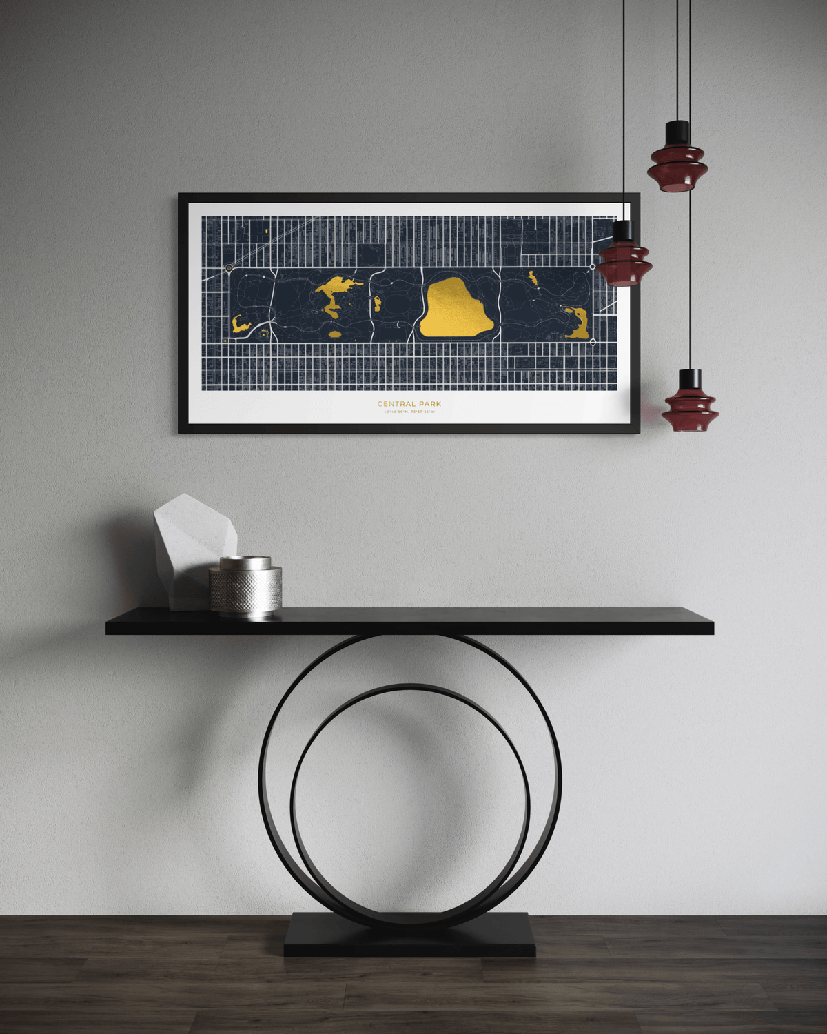 A framed art print featuring a stylized map of New York City in GOLD and dark blue on a white background, hanging on a light gray wall above a black console table with a circular metal base. Red pendant lights hang on the right, and a dark wood floor is visible at the bottom.