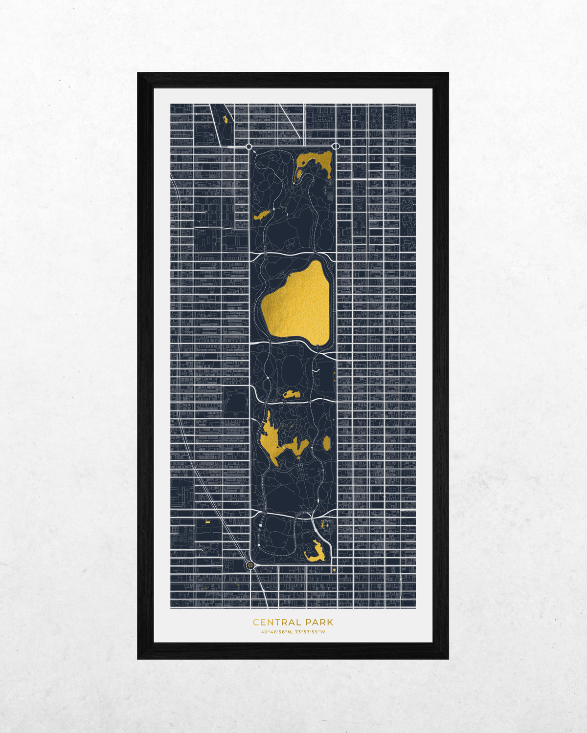 A framed vertical map print of Central Park, New York City, featuring dark navy blue street grid lines with bright gold highlights for the park's lakes and a white mat and black frame, displayed against a light gray textured wall.