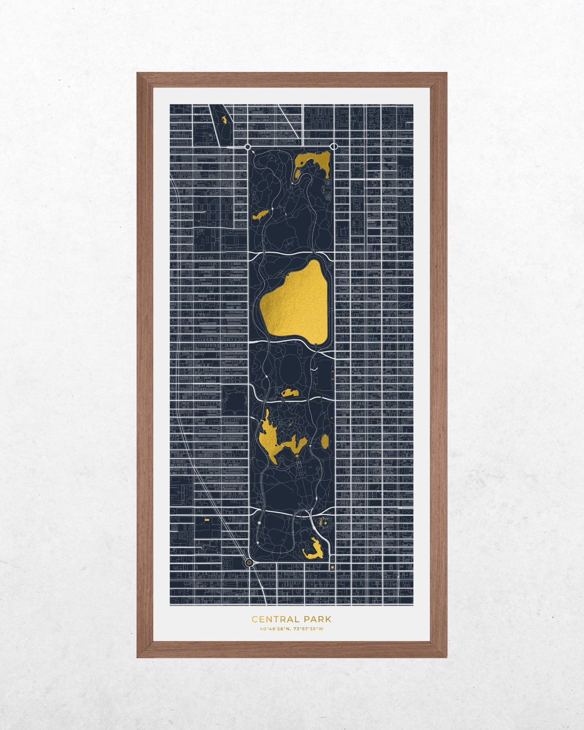 A framed art print of a street map of Central Park, New York City, featuring dark navy blue blocks with bright gold highlights for the park's lakes and paths, set in a light brown wood frame against a textured white wall.