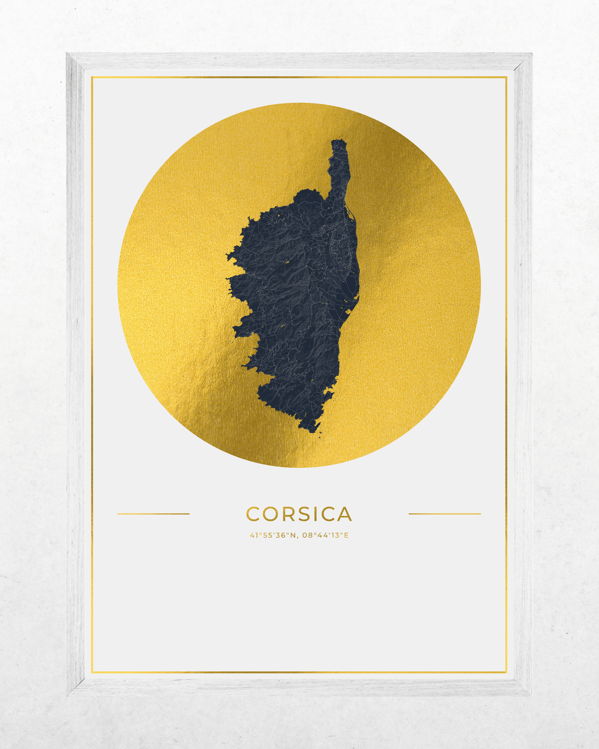 A framed minimalist art print featuring a textured gold circle with a dark navy blue silhouette map of Corsica, with the word 'CORSICA' and coordinates printed below, set in a white frame against a light textured wall.