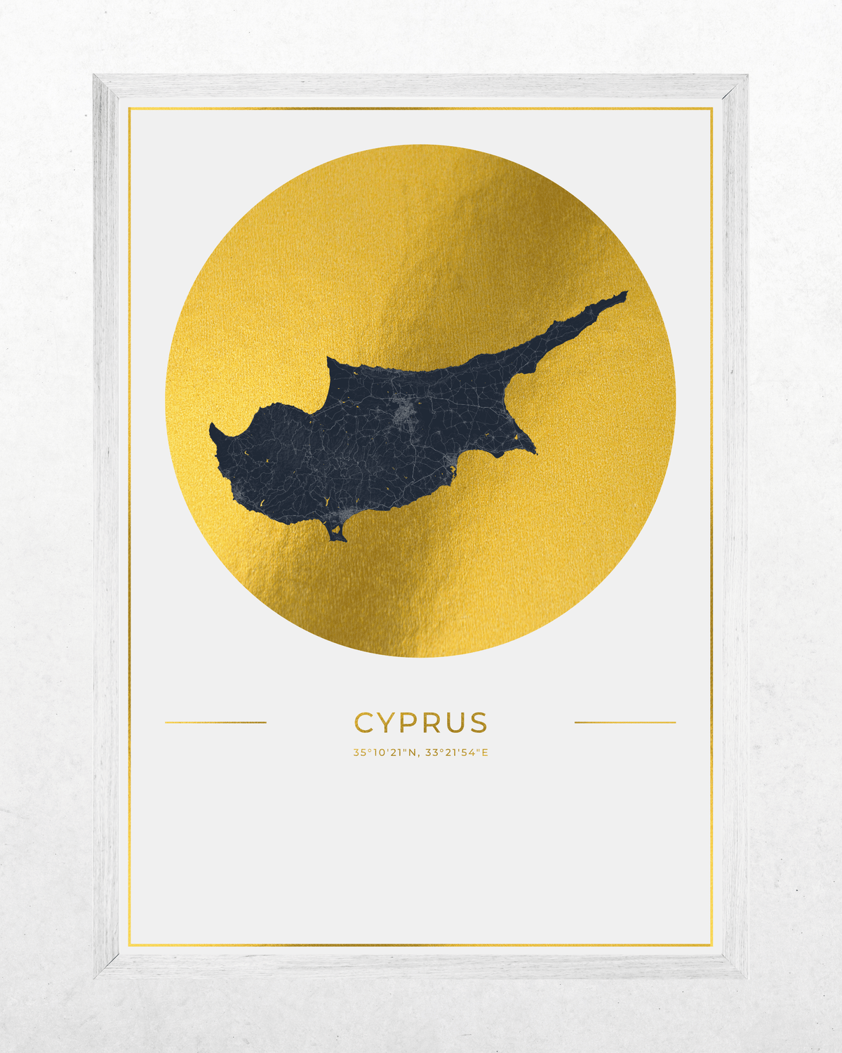 Framed wall art print featuring a dark navy silhouette map of Cyprus centered inside a large textured gold circle on a white background, with the word 'CYPRUS' and coordinates printed below. The print is housed in a white frame and photographed against a light neutral wall.