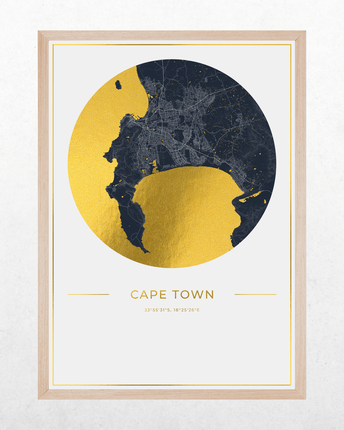 A framed minimalist map print of Cape Town, featuring a circular gold and navy blue design with the city name and coordinates printed below, set in a light wood frame against a textured off-white background.