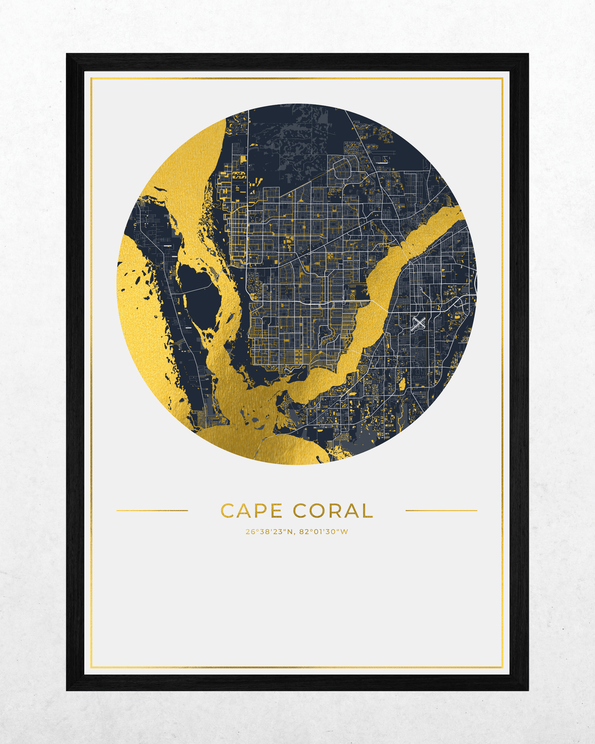 A framed circular map print of Cape Coral, Florida, featuring a navy blue and gold map design with the city name and coordinates printed below, set in a black frame against a light textured background.