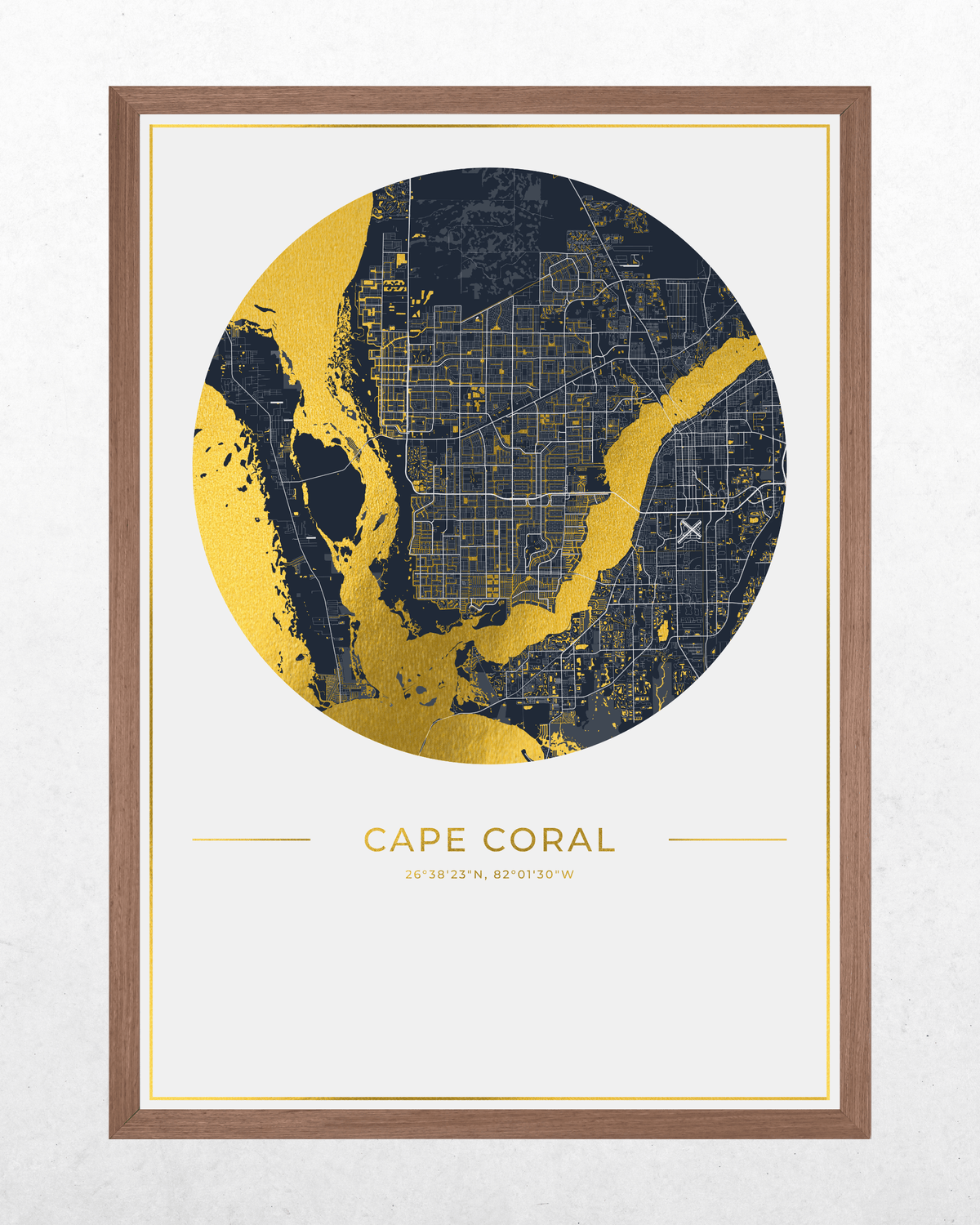 Framed circular city map print of Cape Coral, Florida, featuring a navy and gold street map design with the city name and coordinates printed below, set in a light brown wood frame against a textured white wall.