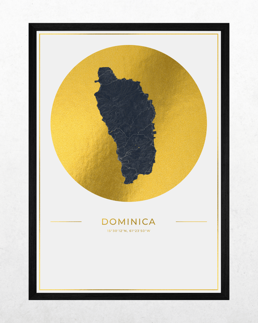 A framed art print featuring a dark charcoal map silhouette of the island of Dominica centered inside a large textured gold circle, with the word 'DOMINICA' and coordinates printed below on a white background. The print is enclosed in a thin white mat and a black frame, shown against a light gray wall.