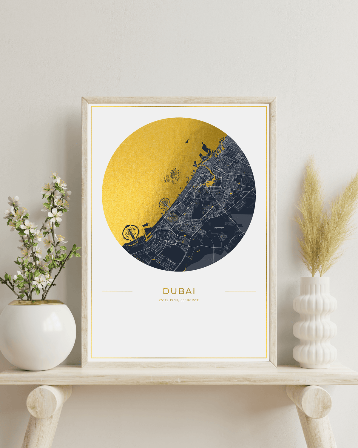 A framed art print of a Dubai street map featuring a large gold circle over a dark blue map design, styled on a wooden shelf with decorative plants.
