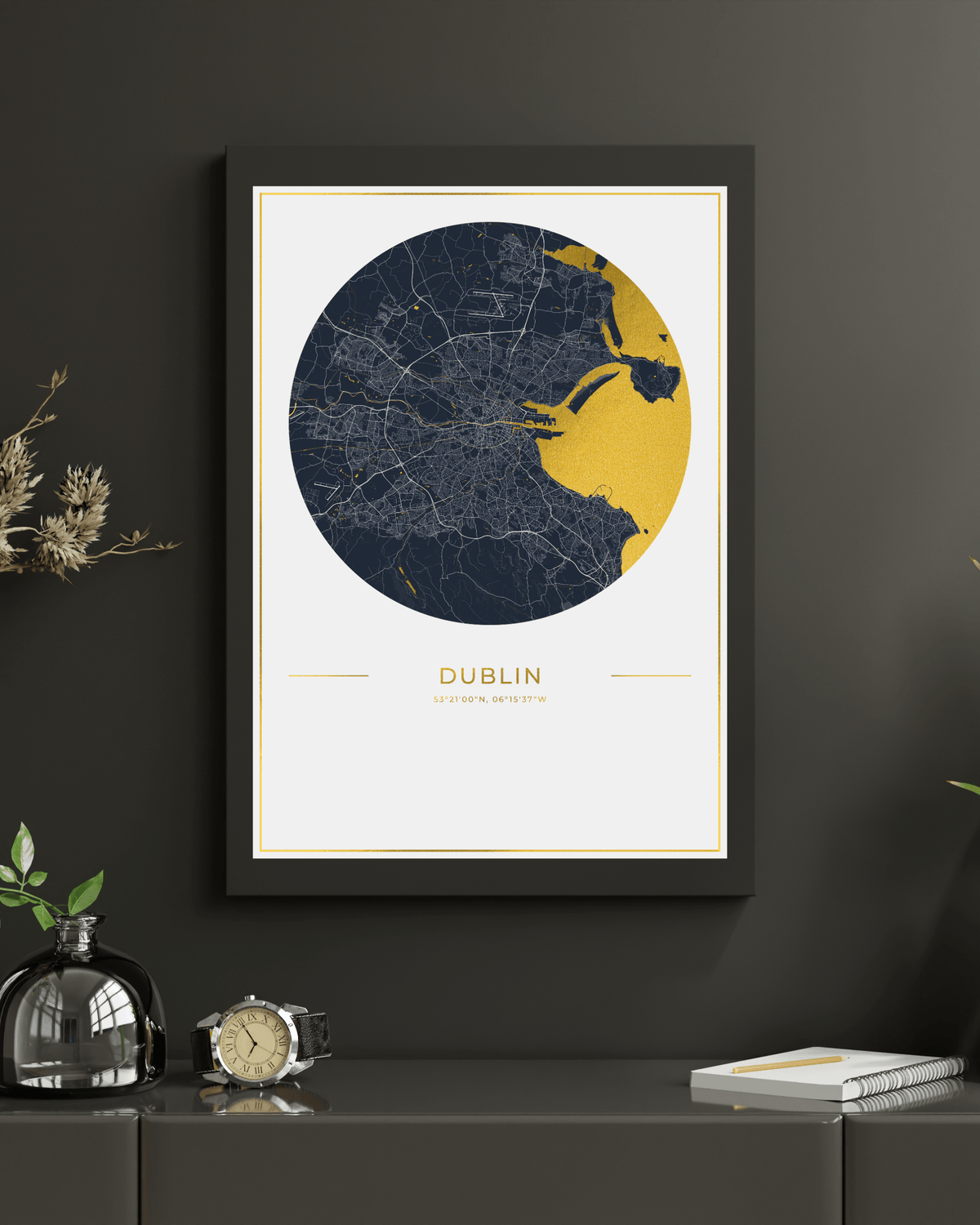 A framed circular city map print of Dublin, Ireland, featuring a navy and gold map design on a white background with gold text, displayed on a dark gray wall above a console table with decorative items.