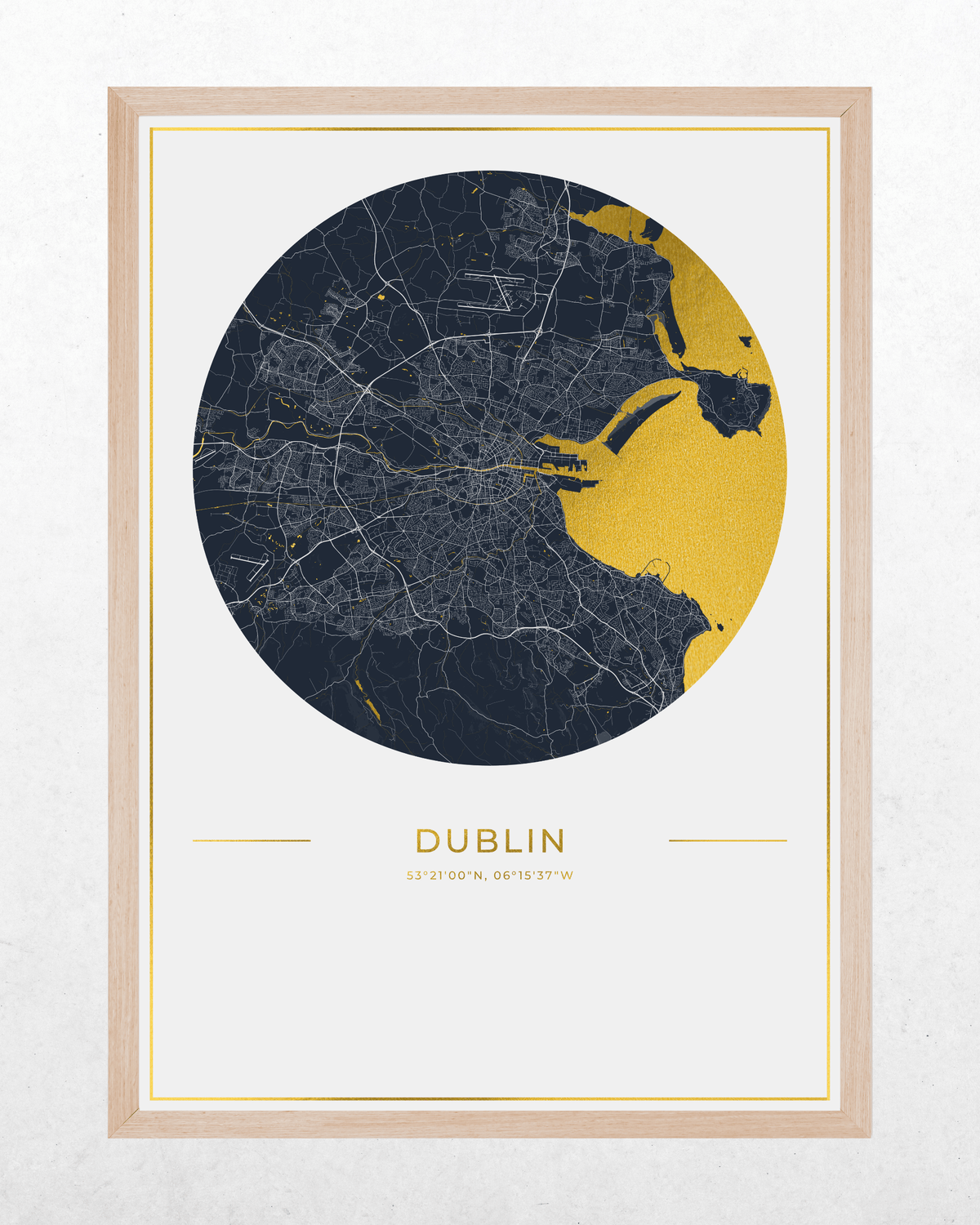 A framed circular city map print of Dublin, featuring a dark navy street network with a gold highlighted coastal area and city outline, plus the word DUBLIN and coordinates below, shown in a light wood frame against a light textured wall.