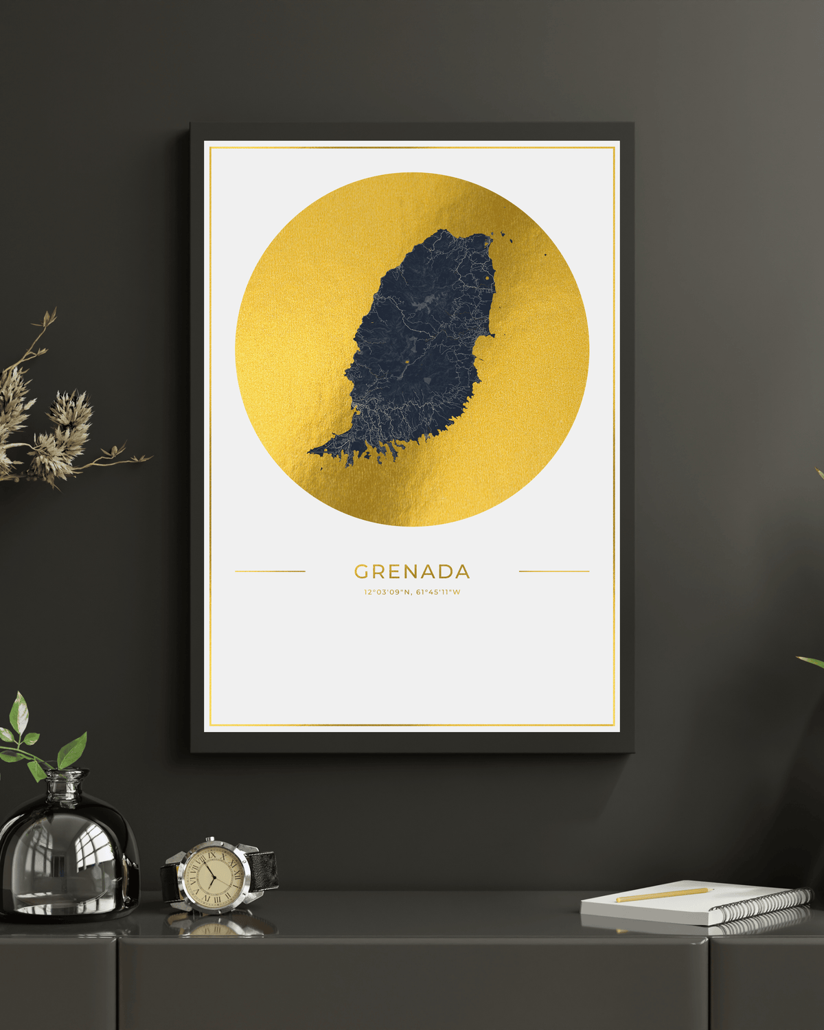 Framed wall art featuring a stylized map of Grenada in dark navy blue inside a large gold circle, displayed on a dark gray wall above a console table with decorative objects.