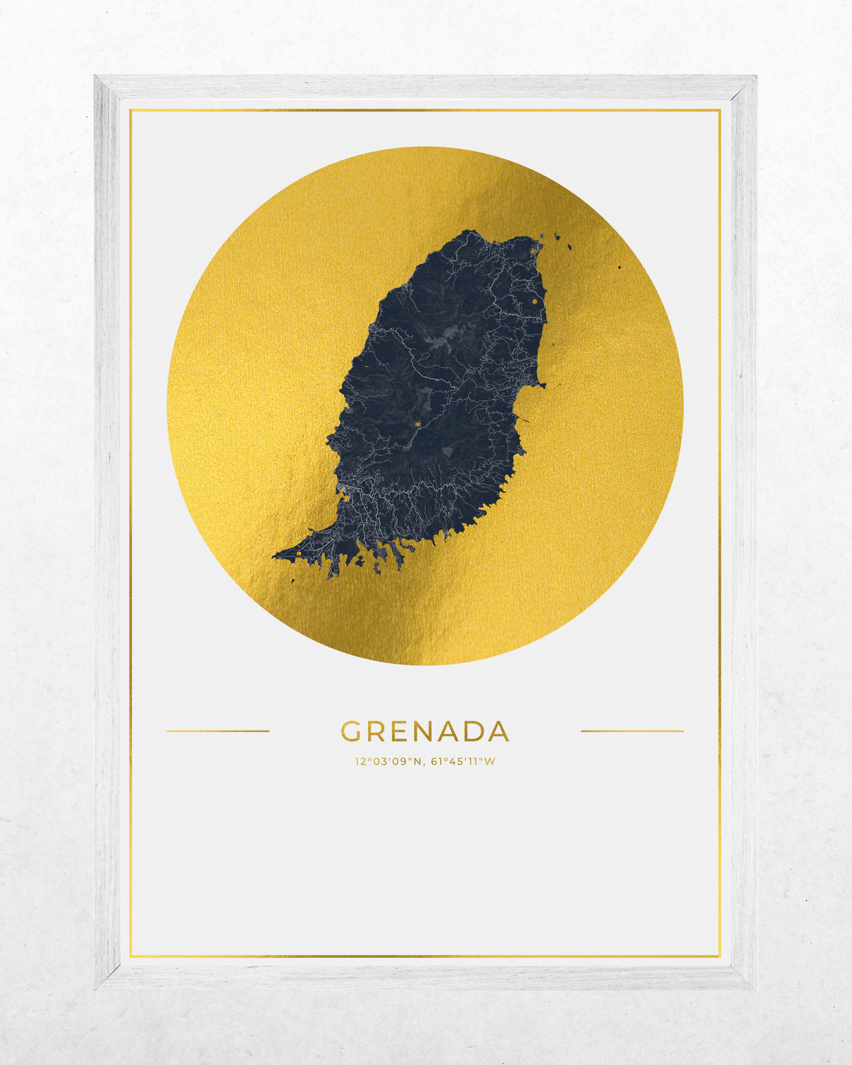 A framed art print featuring a dark navy map silhouette of Grenada centered inside a large textured gold circle, with the word GRENADA and coordinates printed below on a white background. The print is housed in a light gray wood frame and photographed against a light gray wall.