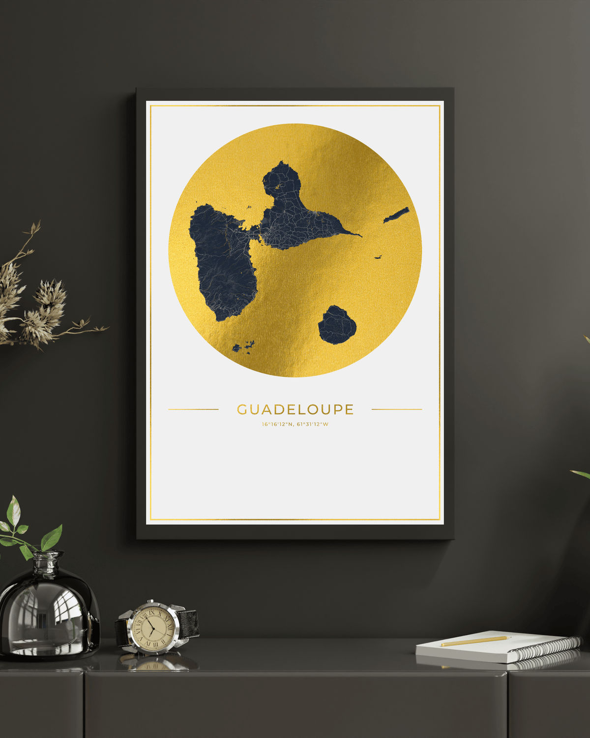 Framed wall art featuring a gold map of Guadeloupe with dark blue landmasses, displayed on a dark gray wall above a console table with decorative objects.