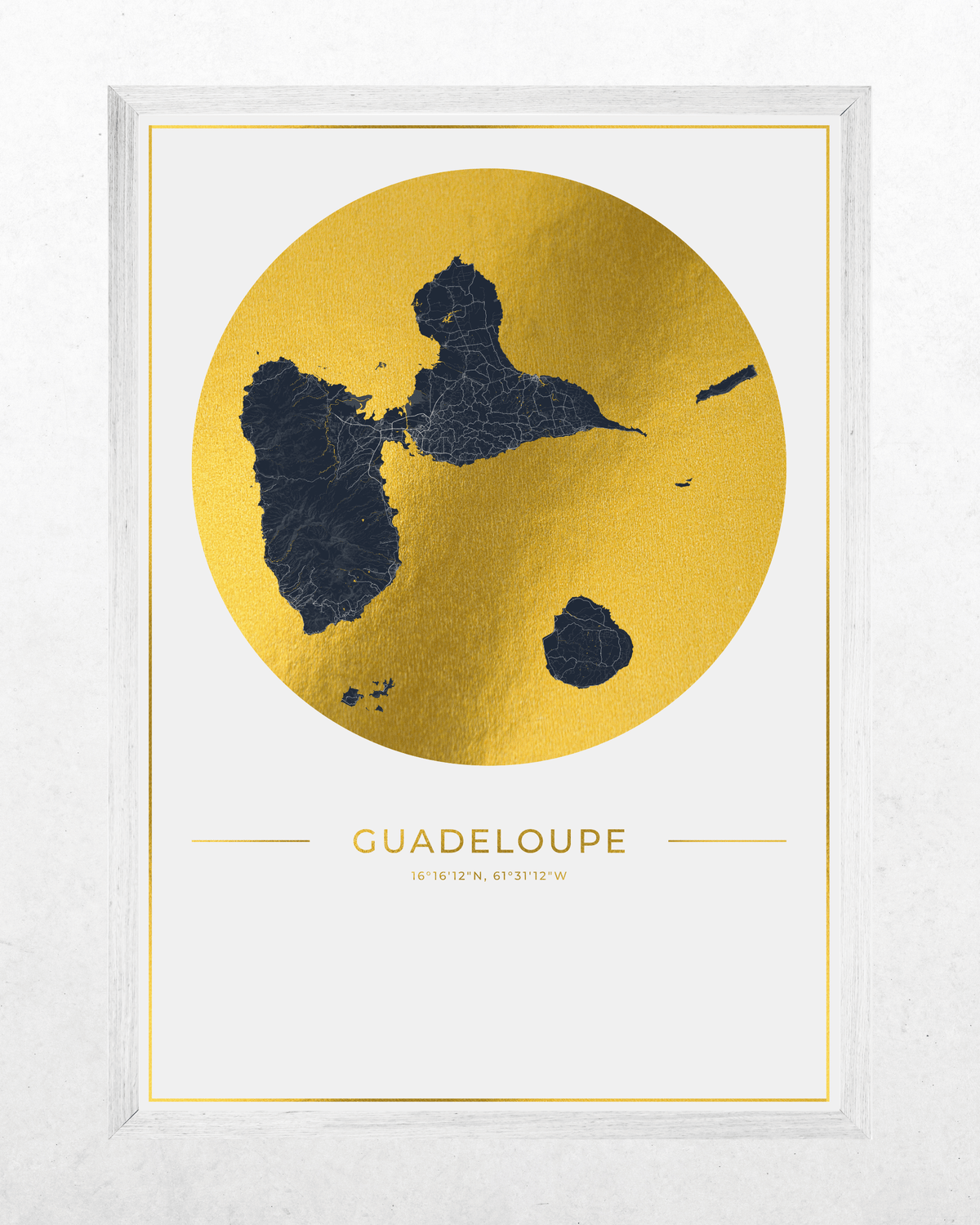 Framed wall art print featuring a stylized map of Guadeloupe in dark navy blue inside a large metallic gold circle, with the word 'GUADELOUPE' and coordinates printed below, shown in a white frame against a light textured background.