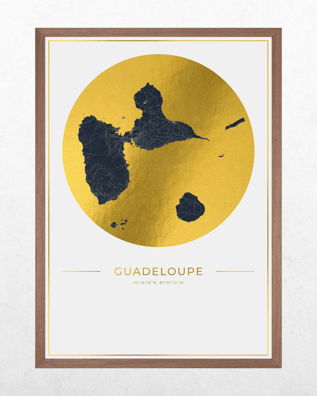 Framed Guadeloupe map art print with a large gold circular shape and dark navy landmasses, shown in a brown wood frame against a light textured wall.