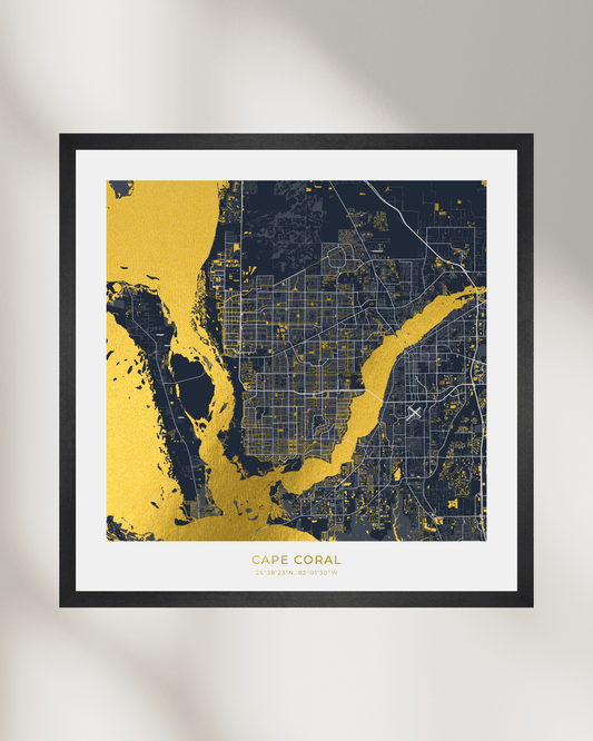 Framed wall art featuring a stylized map of Cape Coral, Florida, with gold waterways and dark navy land, shown in a black frame against a light gray wall with soft shadowing.