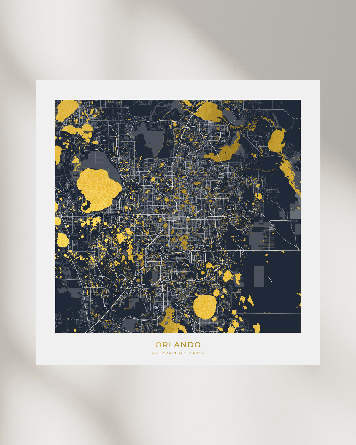 A framed city map print of Orlando, Florida, featuring a dark navy blue background with gold foil highlighted areas and white street lines, displayed against a soft beige background with subtle shadows.