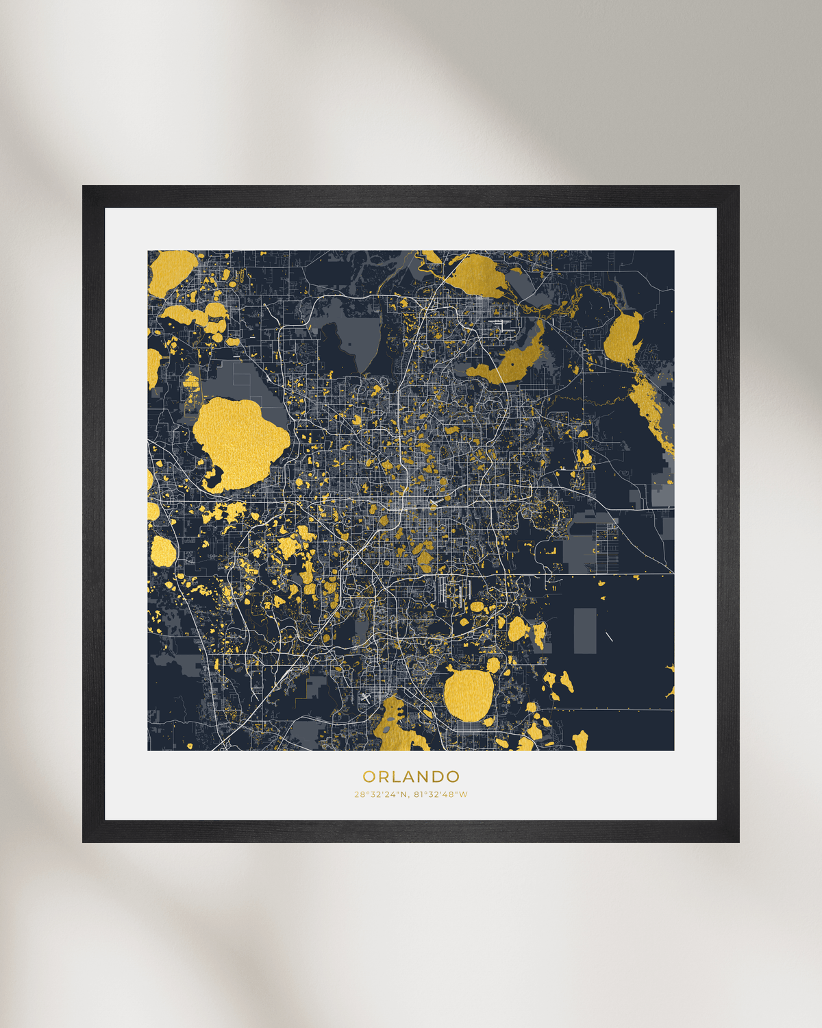 Framed city map print of Orlando, Florida, featuring a dark navy and gray map design with gold highlights, set in a black frame with a white mat against a light gray wall.