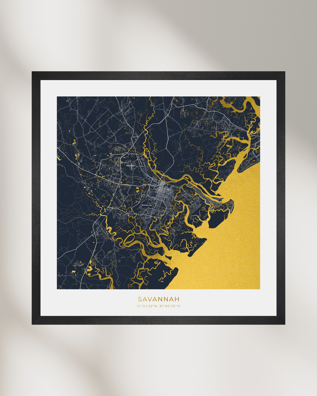 Framed Savannah city map art print with a black frame, white mat, and a navy, gold, and gray map design on a light gray background.
