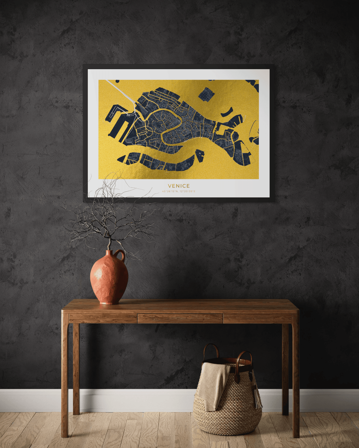 A framed Venice street map art print in gold and navy blue hangs on a dark textured wall above a wooden console table with a terracotta vase and a woven basket.
