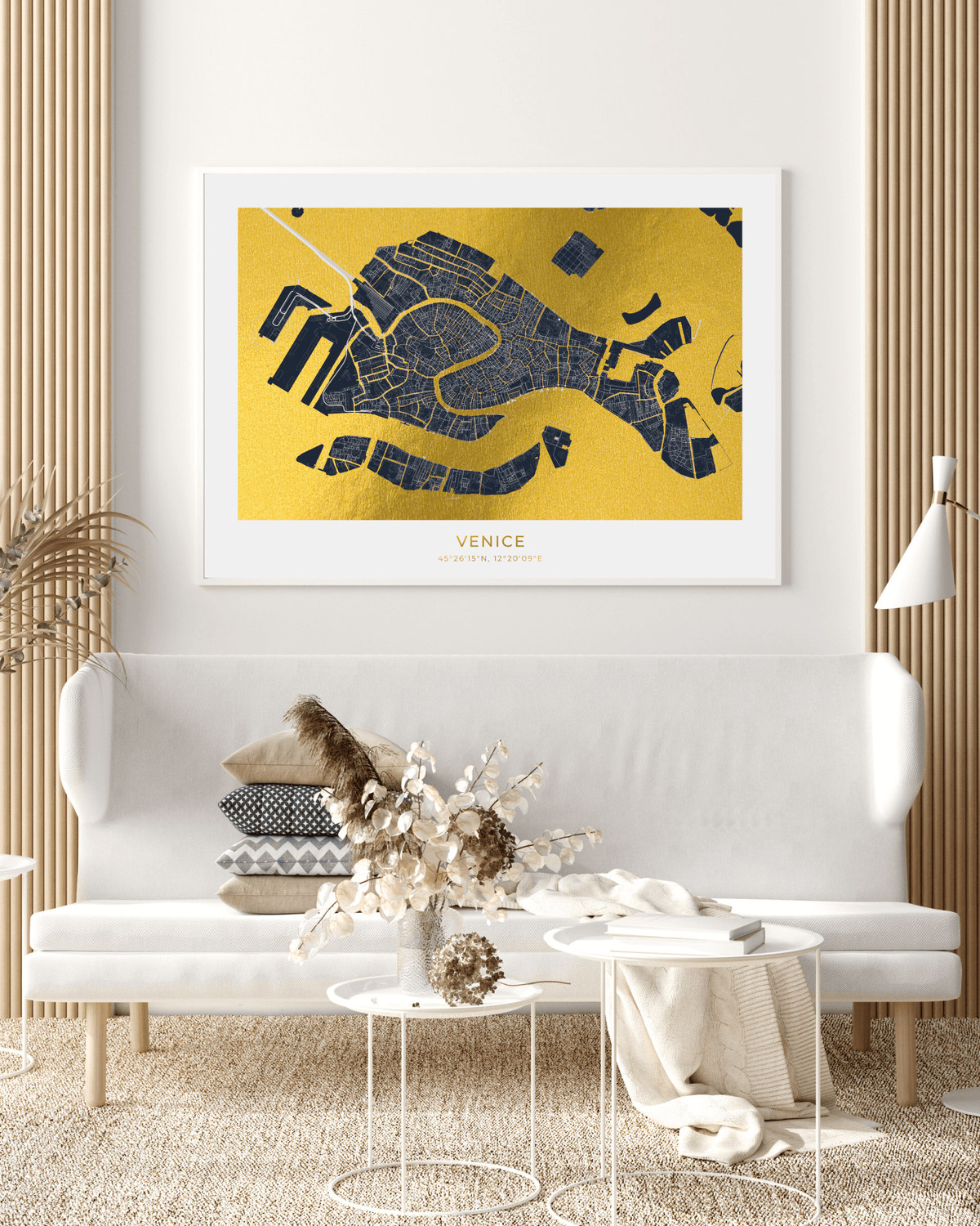 A framed Venice city map art print in gold and navy blue hangs on a white wall above a modern white sofa in a styled living room setting.