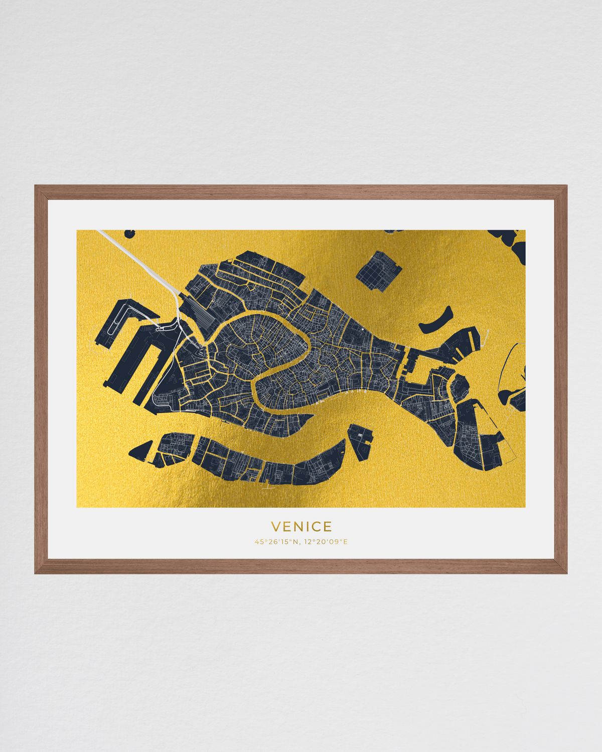 A framed map print of Venice, Italy, featuring a dark navy blue street layout on a textured gold background, enclosed in a white mat and a light brown wood frame against a light gray wall.
