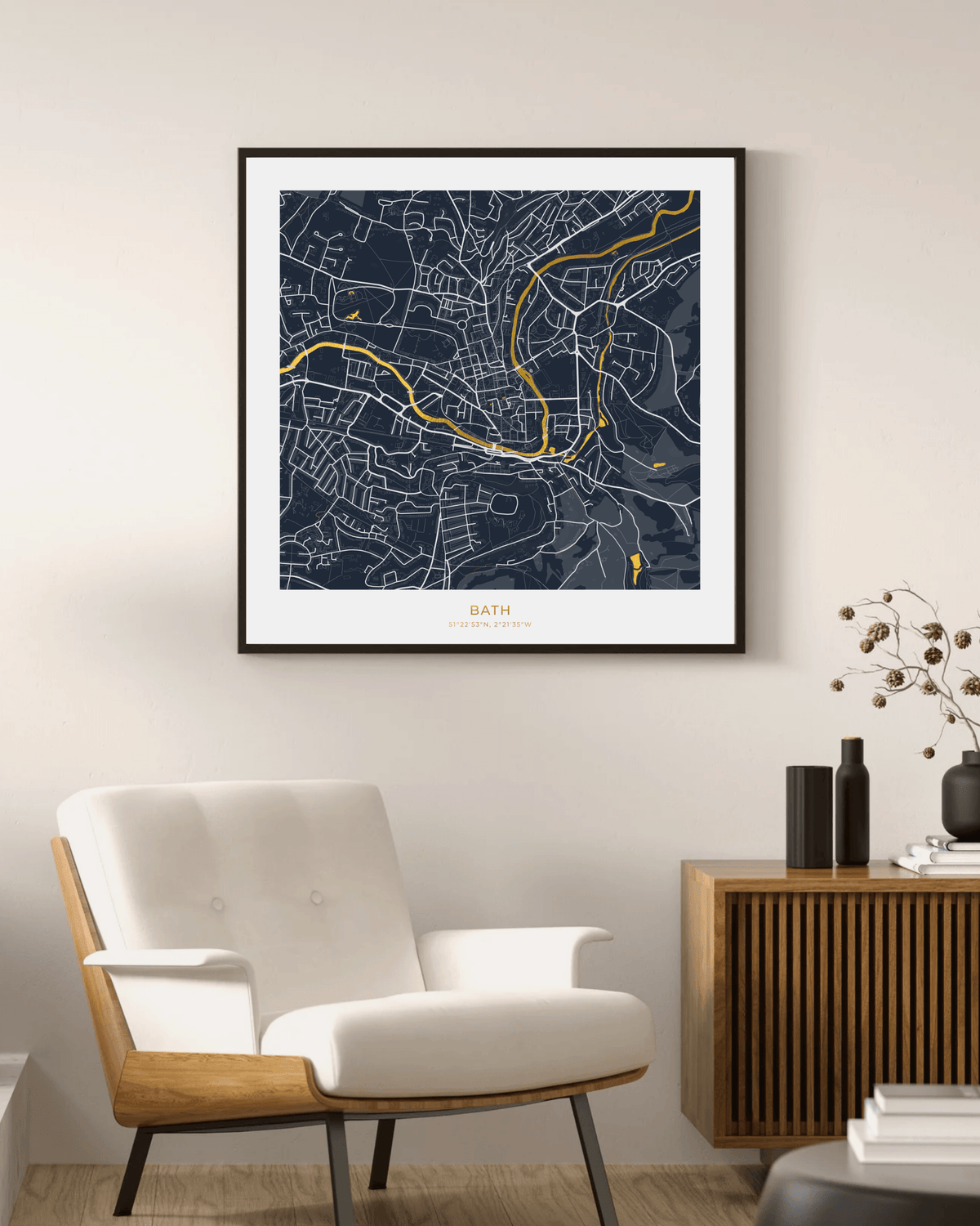 A framed art print of a street map of Bath, UK, styled in a modern living room setting above a white armchair and a wooden sideboard.