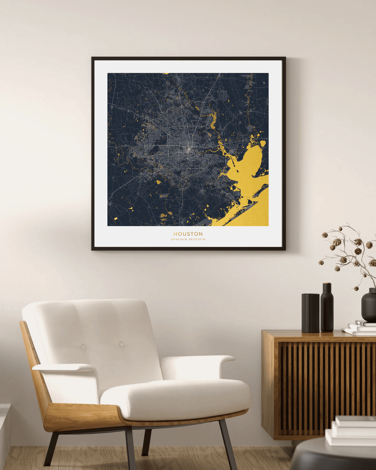 A framed Houston city map art print with a dark navy background and gold highlights, hanging on a light beige wall above a white armchair and a wooden sideboard.