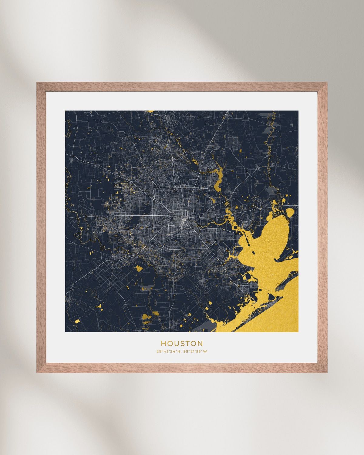 A framed Houston city map art print with a dark navy background and gold highlighted waterways, a white mat, and a thin brown wood frame, shown against a light neutral wall with soft shadows.