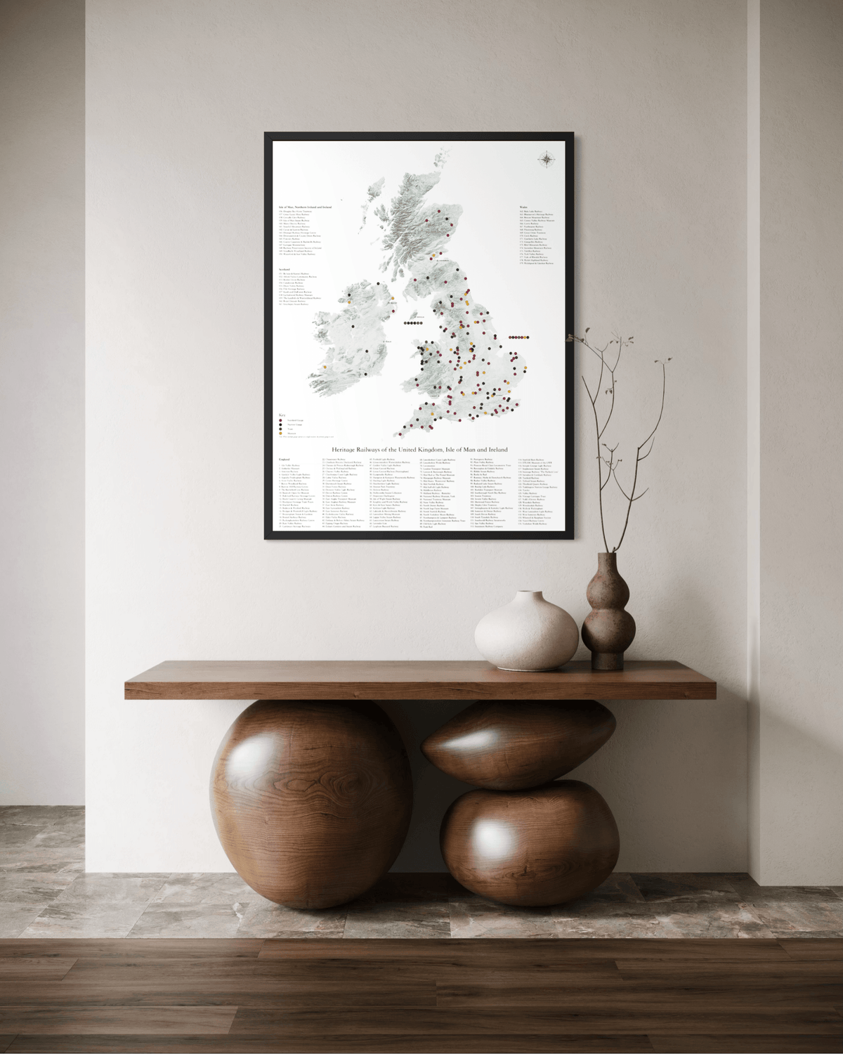 A framed art print of a UK and Ireland map with detailed location markers, displayed on a neutral wall above a wooden console table with decorative ceramic vases and sculptural stone bases.