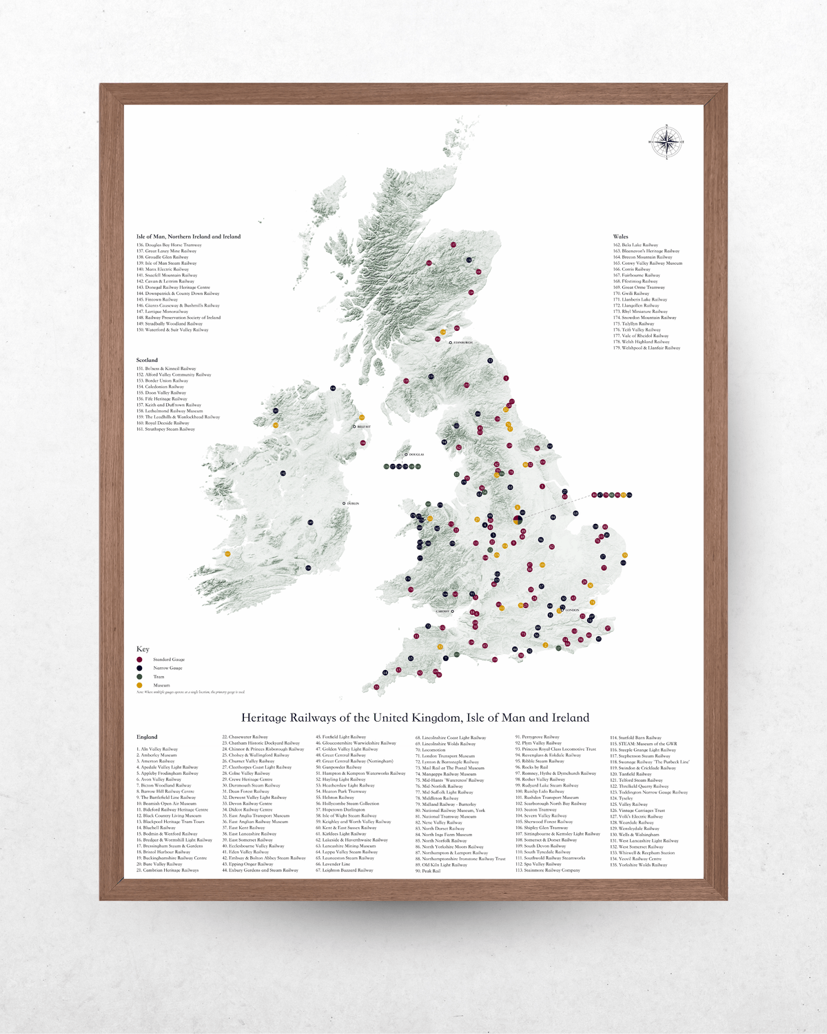 A framed vintage-style map poster of the United Kingdom and Ireland, featuring a detailed map with numerous colored dots marking heritage railway stations, accompanied by extensive station lists at the bottom. The map is housed in a light brown wood frame and displayed against a textured white wall.