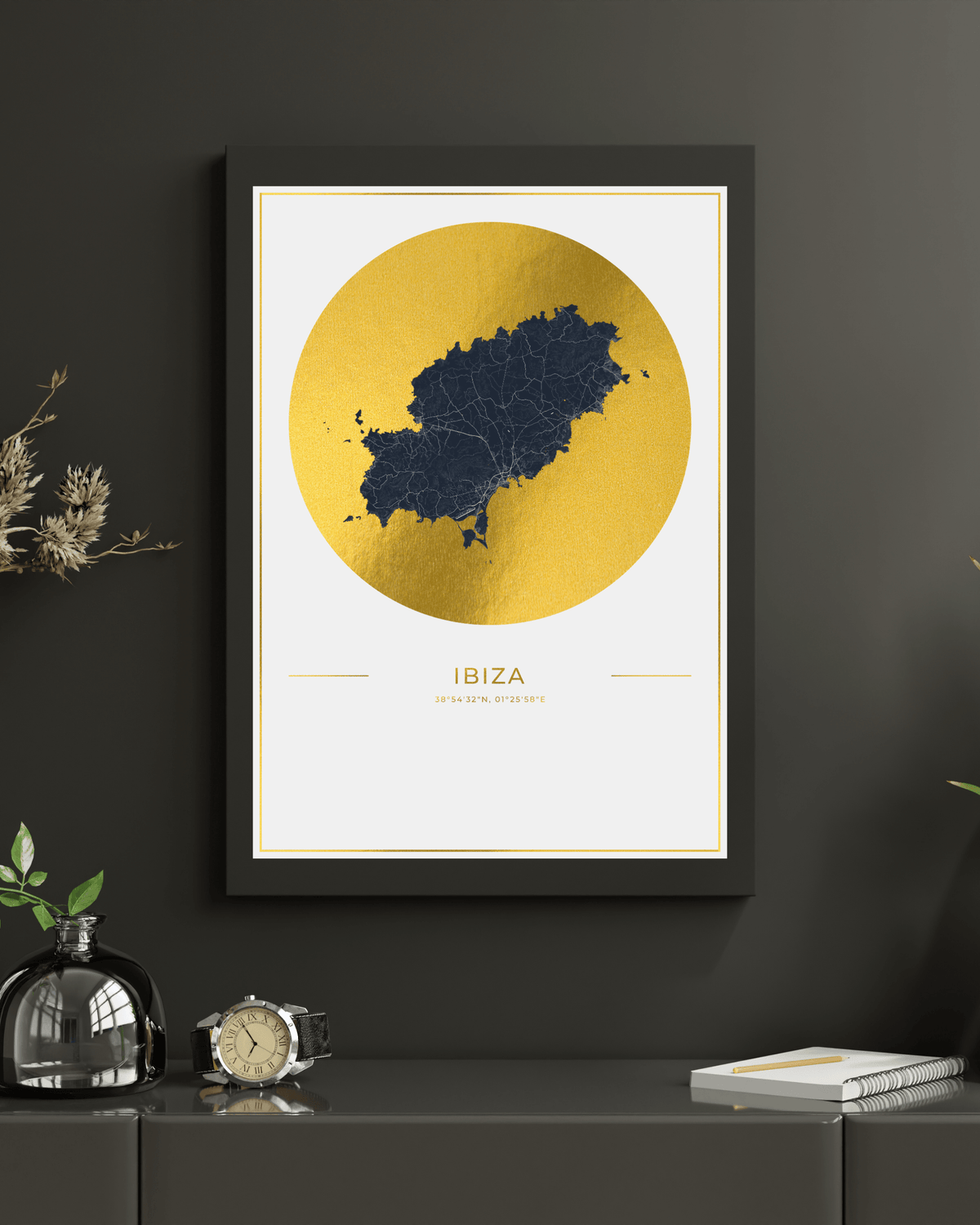 Framed wall art featuring a gold map of Ibiza, Spain, with the word 'IBIZA' and 'MEDITERRANEAN ISLAND' printed below, displayed on a dark gray wall above a console table with decorative objects.