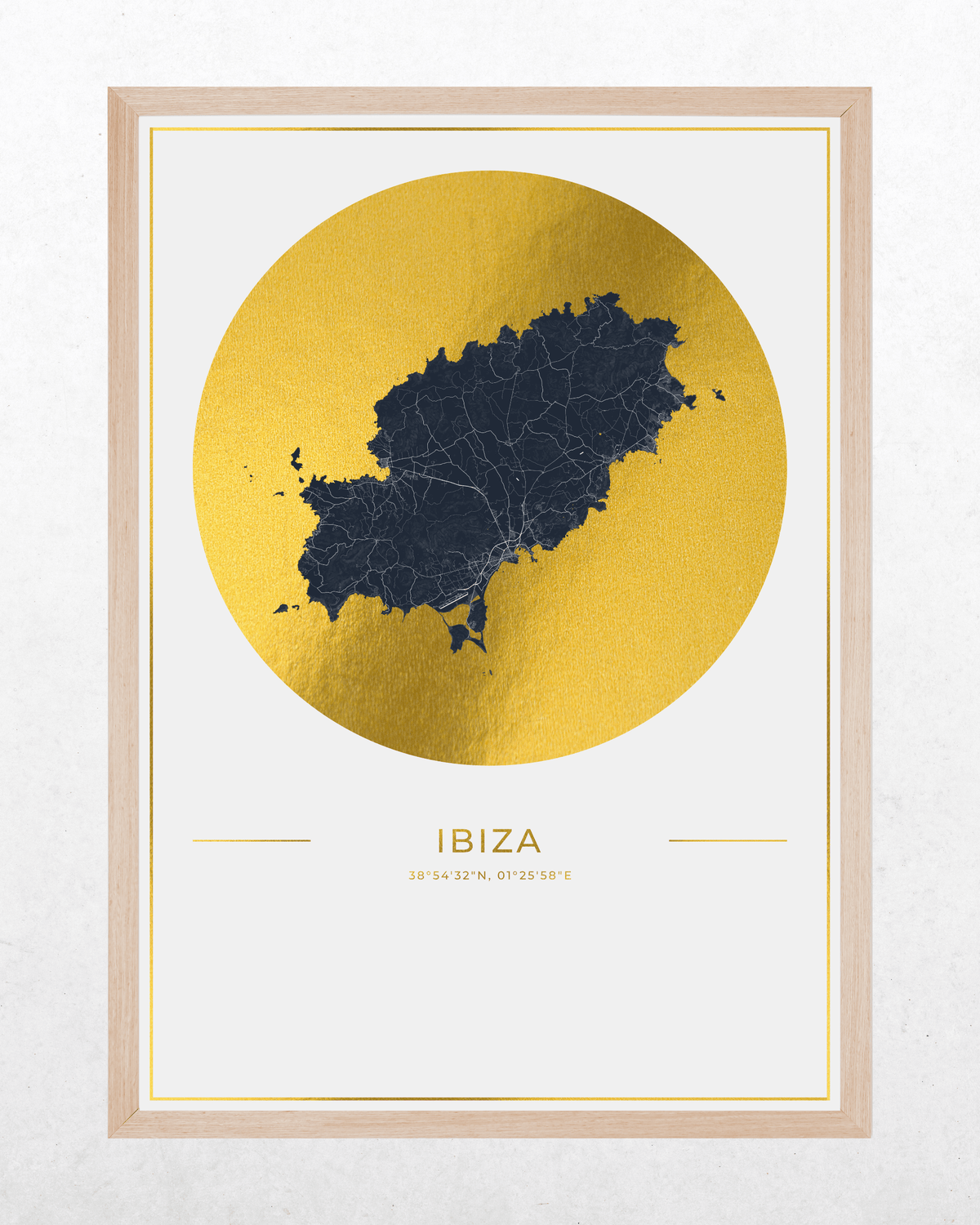 A framed minimalist art print of Ibiza, featuring a dark navy blue map silhouette centered inside a large textured gold circle, with the word 'IBIZA' and coordinates printed below. The print is housed in a light natural wood frame and displayed against a light gray textured wall.