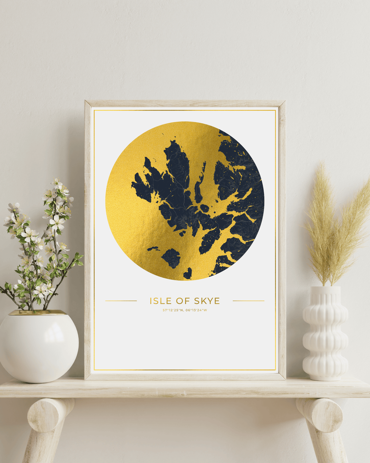 A framed art print of the Isle of Skye, Scotland, featuring a textured gold circular map with a dark blue silhouette of the islands, styled on a light wood shelf with decorative vases.