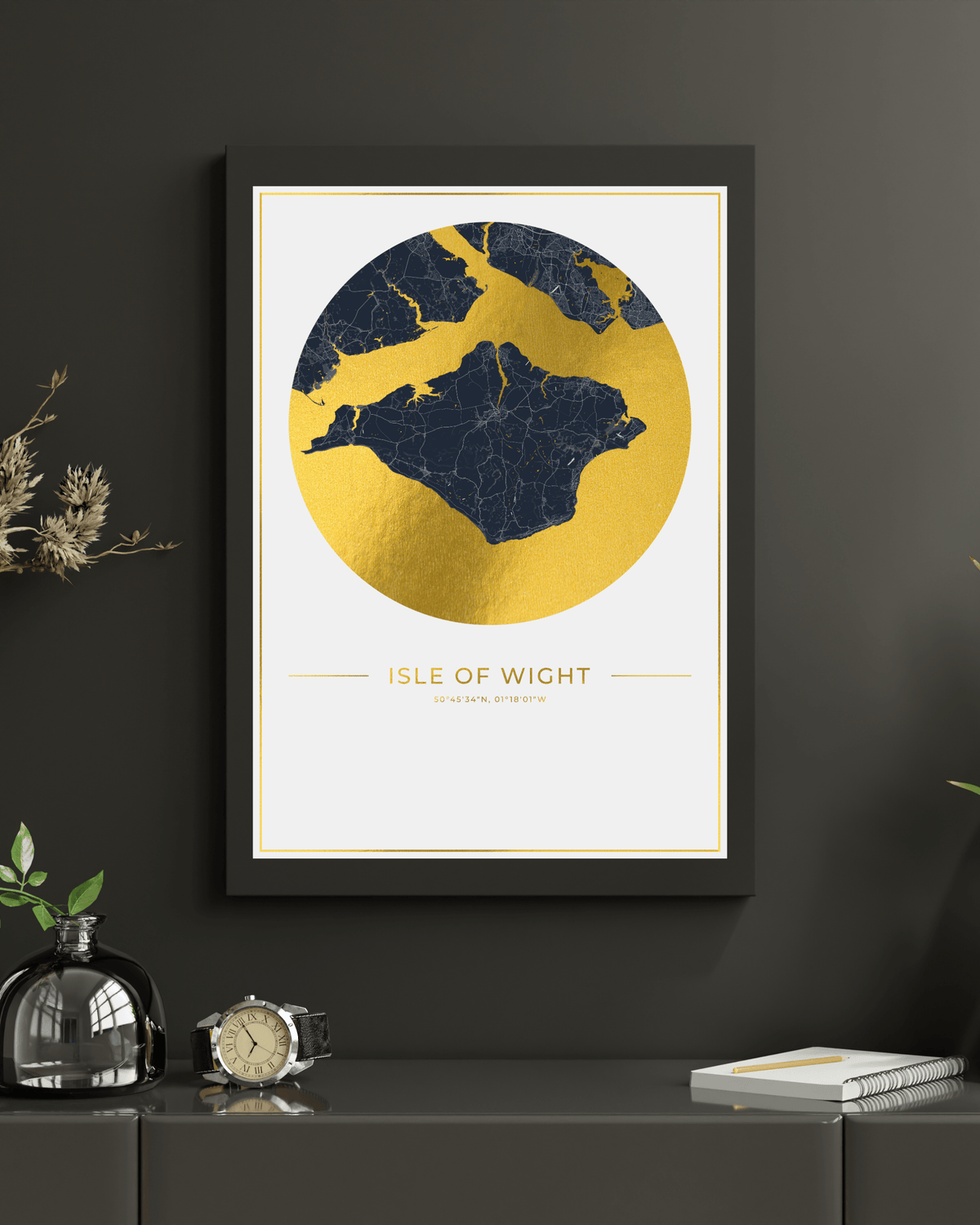 A framed art print featuring a gold and navy map of the Isle of Wight, displayed on a dark gray wall above a console table with decorative items.
