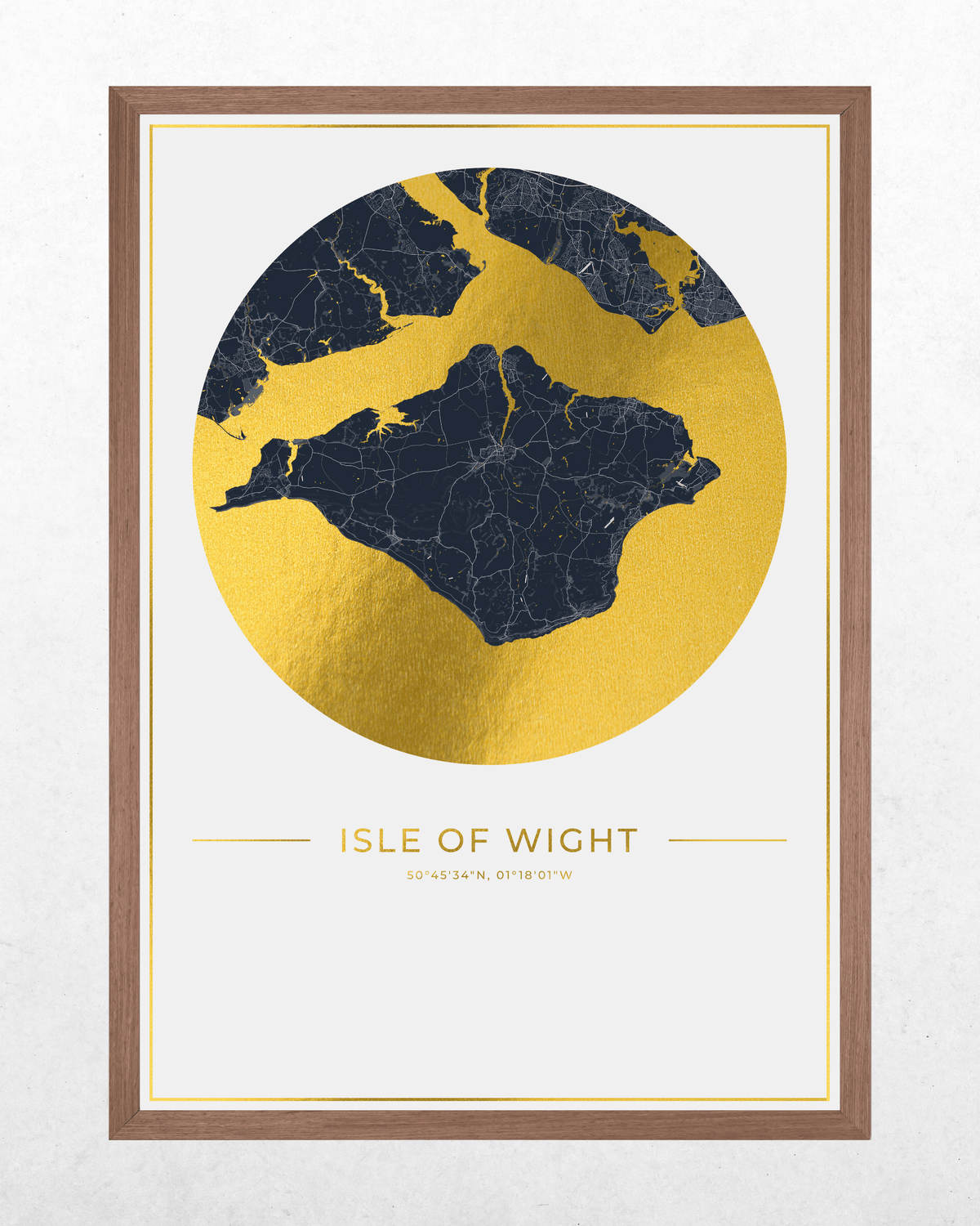 Framed wall art print featuring a stylized map of the Isle of Wight, with a large gold circular landmass and dark navy waterways, plus the text 'ISLE OF WIGHT' and coordinates below, shown in a brown wood frame against a light textured wall.